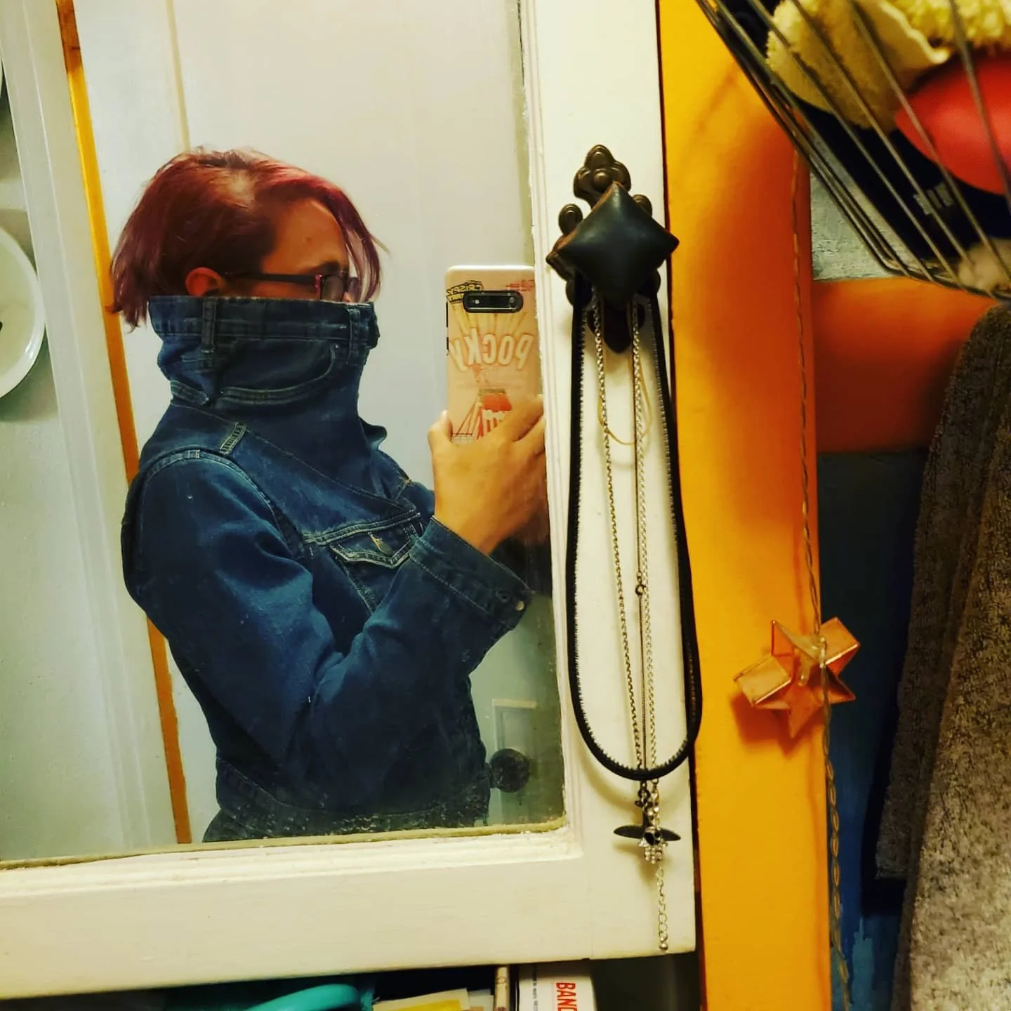 mirror selfie of a red-haired woman wearing a denim vest over a denim shirt with a collar that covers half her face. The collar is the entire top of some children's jeans