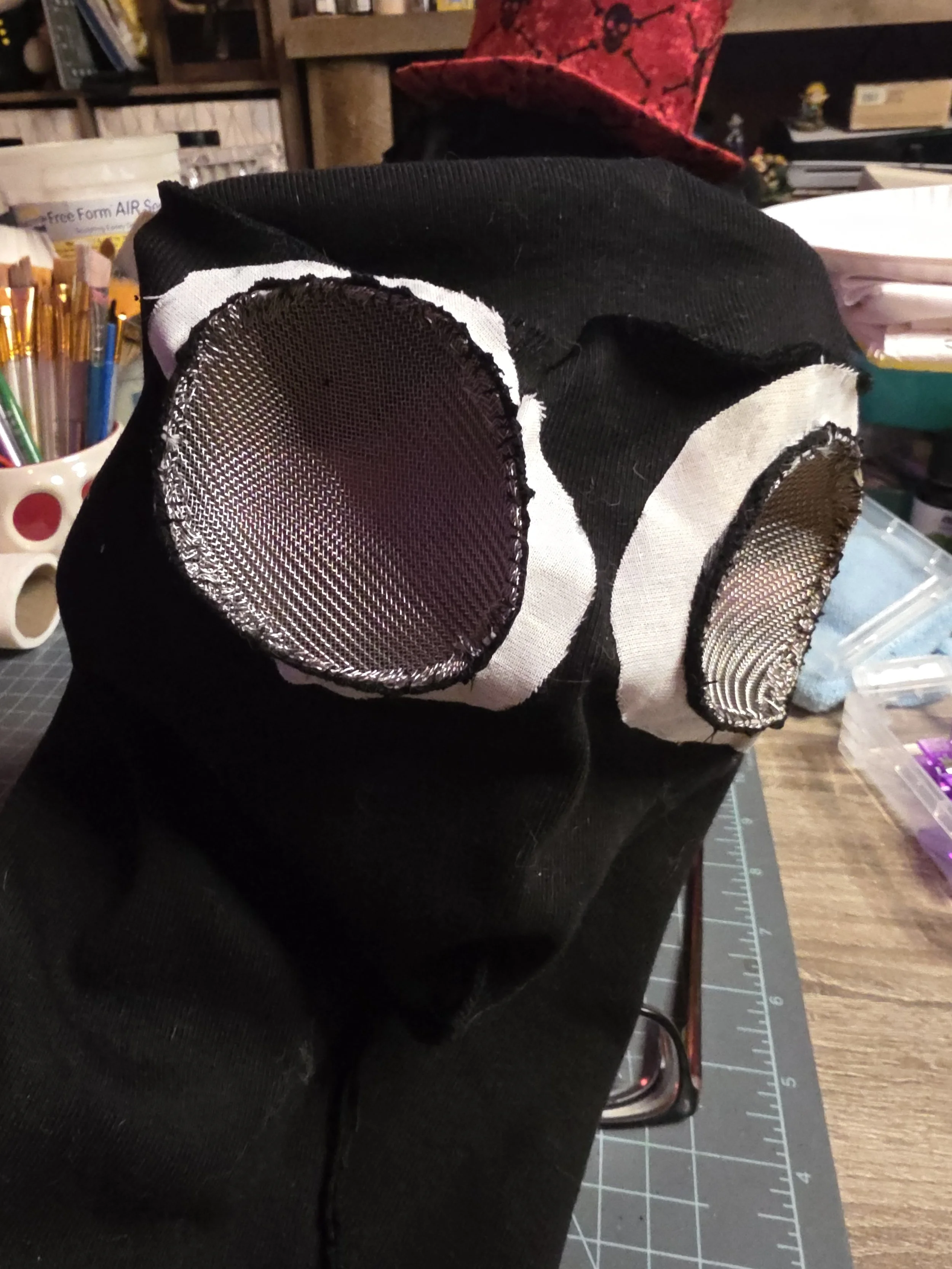 Both eye holes of an inside out ninja hood have metal screen eye guards stitched in. Around each eye is a ring of white fabric interfacing for reinforcement.