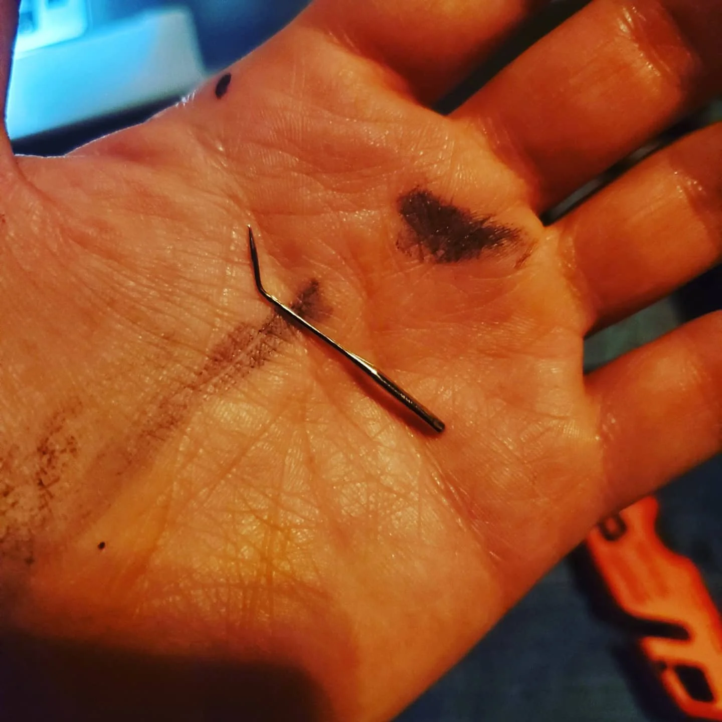 a hand with some paint smudges, holding a bent sewing machine needle in the palm