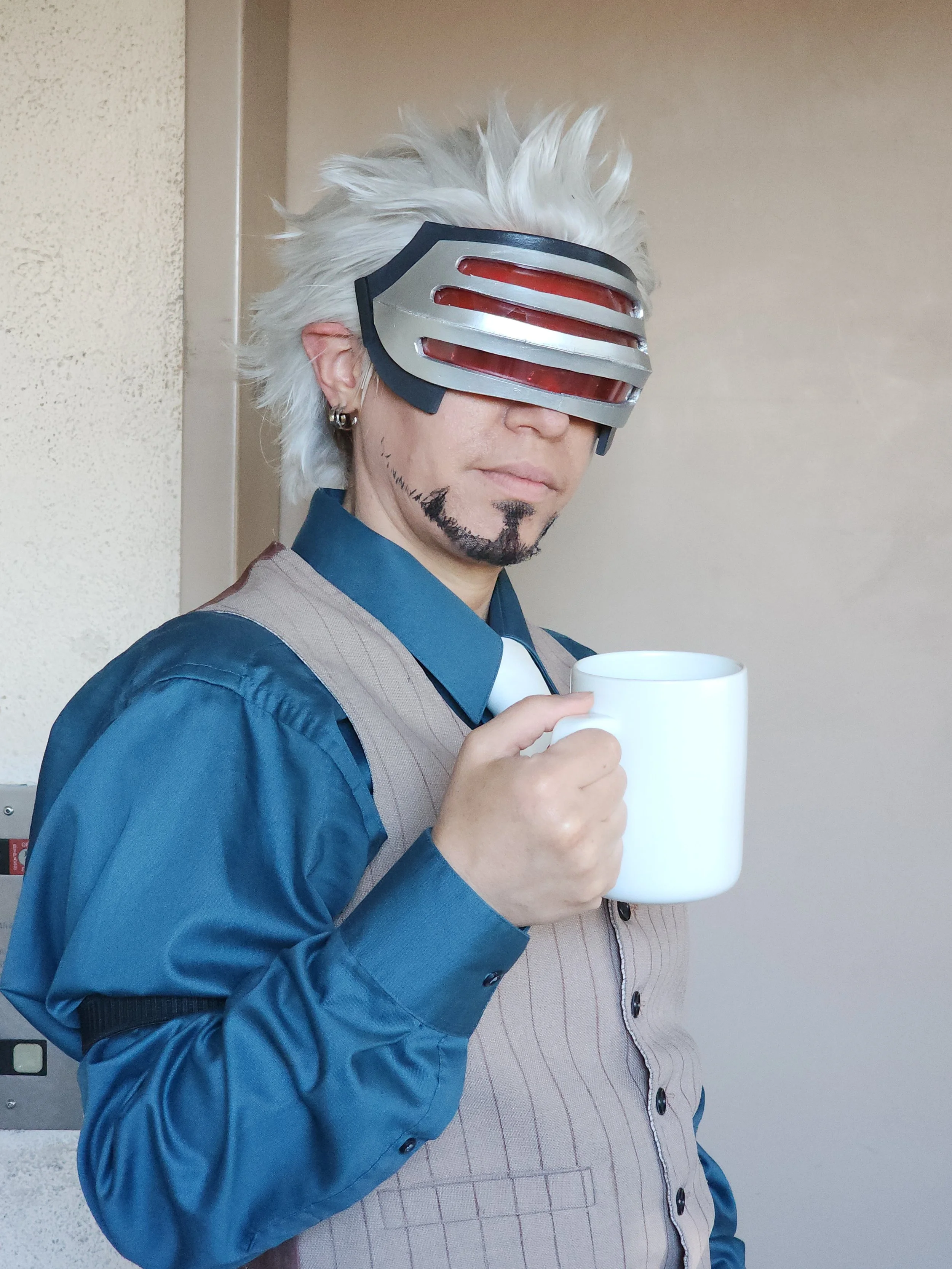 Godot from Ace Attorney Cosplay with a teal button up shirt, tan vest, white spikey wig, holding a coffee cup. A silver visor with 3 long red lenses covers the eyes, and a goatee has been applied and extended with eyeliner along the jaw