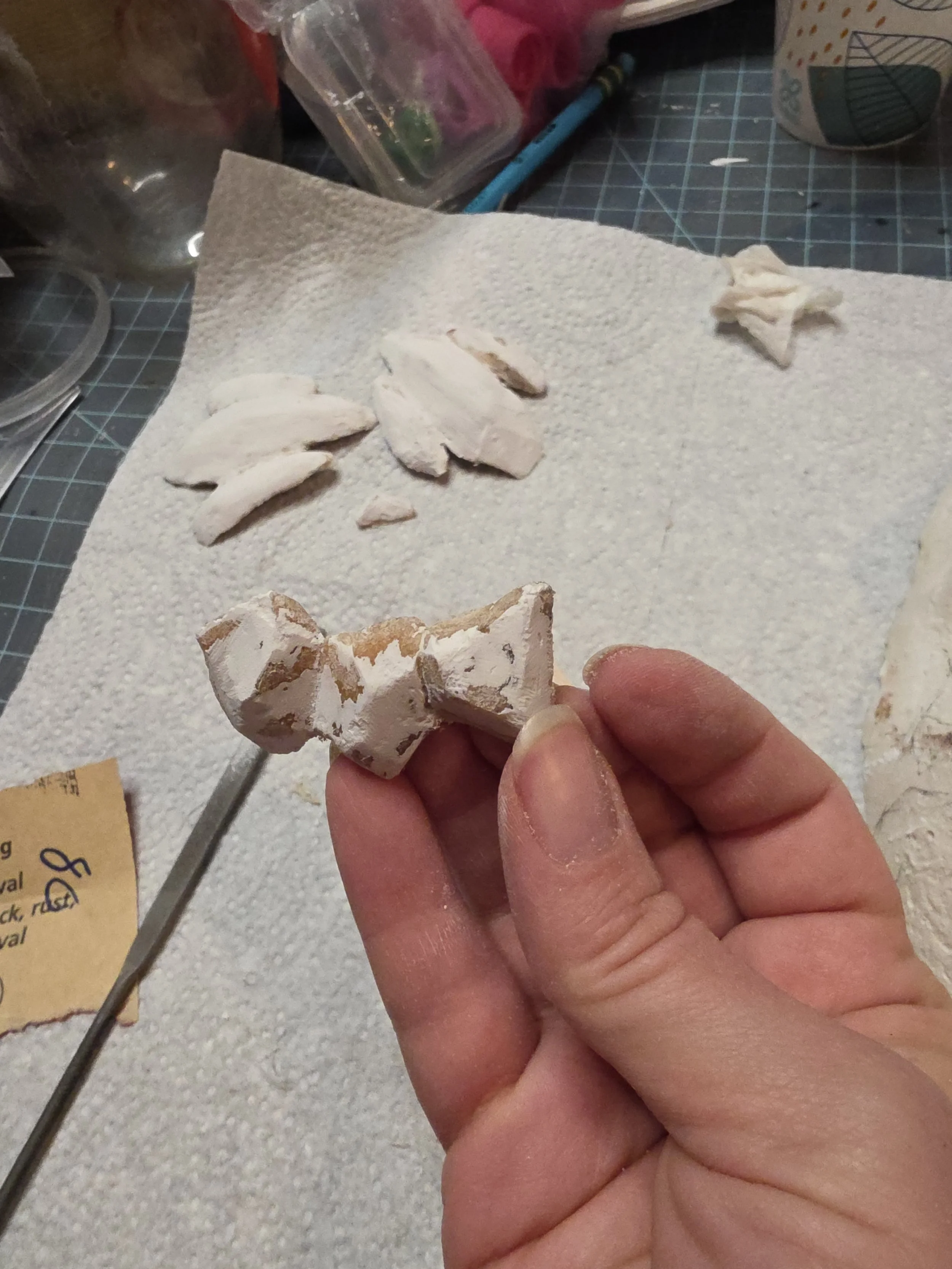 hand holding rock-like scales made of tan worbla, with white gesso that has been sanded into smooth, angular planes