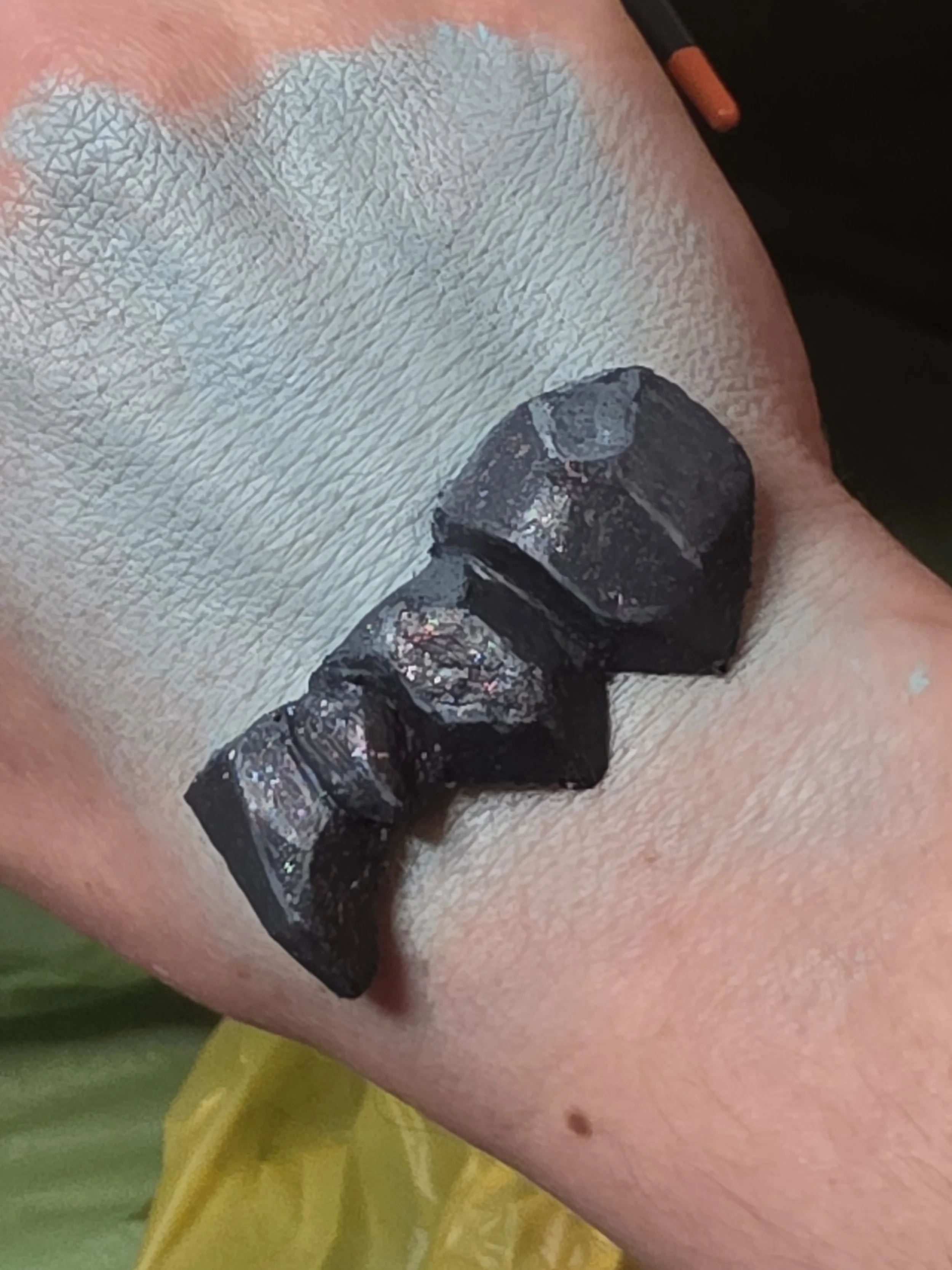 hand with pale blue makeup swatched on the back, and dark blue-gray rocklike scales placed on the wrist