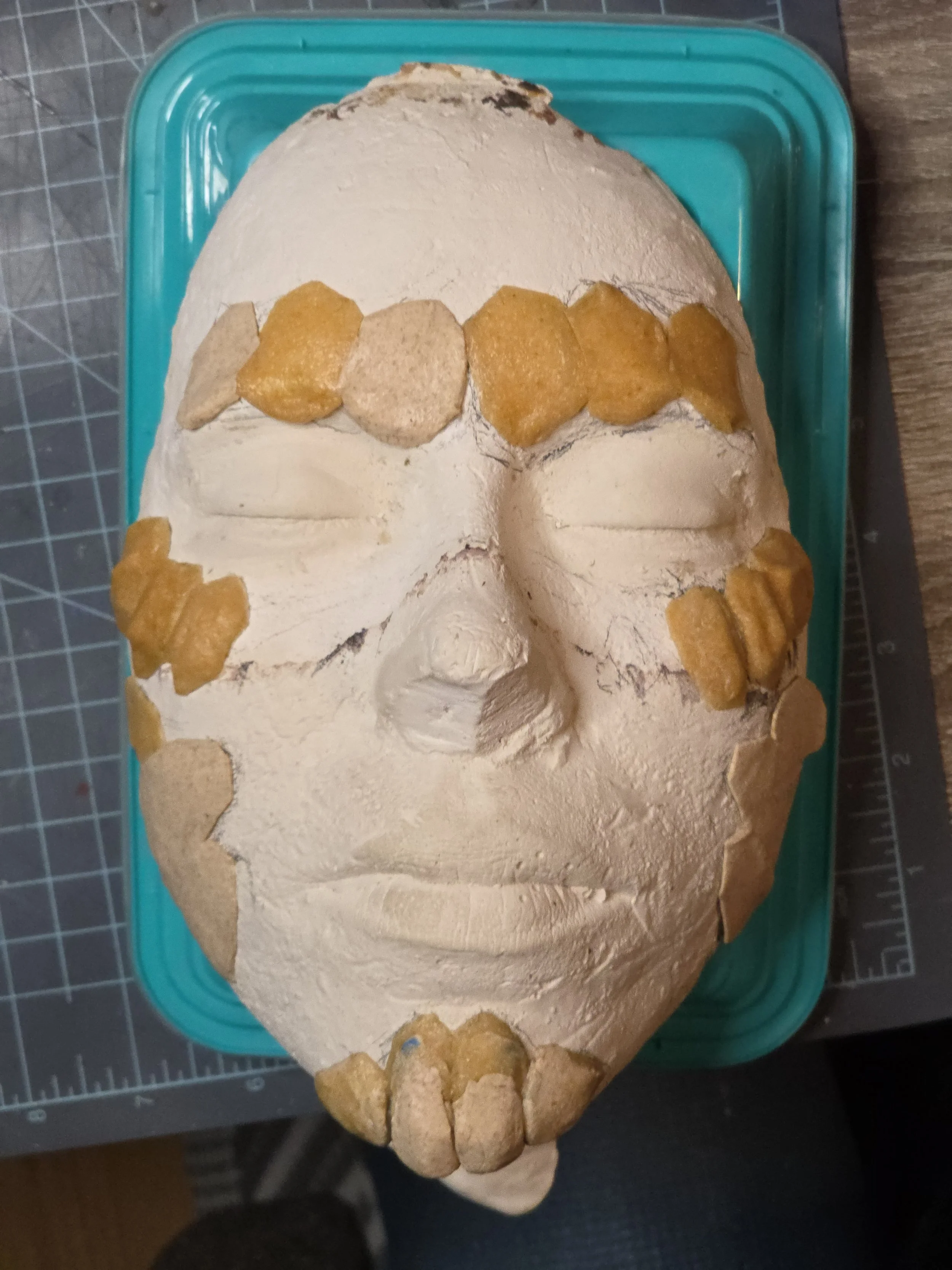 plaster face cast with rocklike scales made of tan worbla, placed over the eyebrows, cheekbones, chin, and jawline