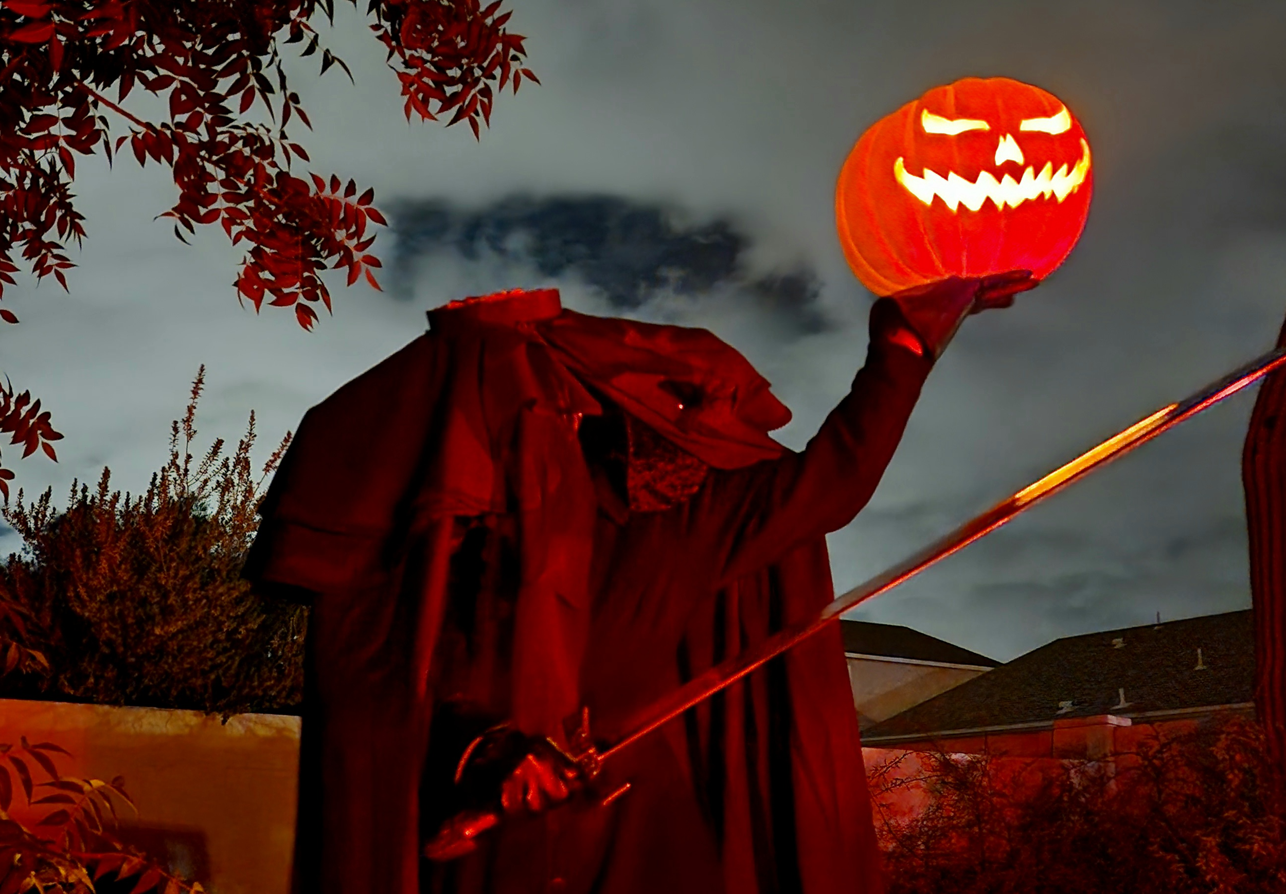 Cosplay of the Headless Horseman holding up a glowing orange jack-o-lantern, with a sword in the other hand. The headless shoulders have a ruffled cape and a lace scarf where the neck is cut off. The sky is dark and cloudy behind the Horseman