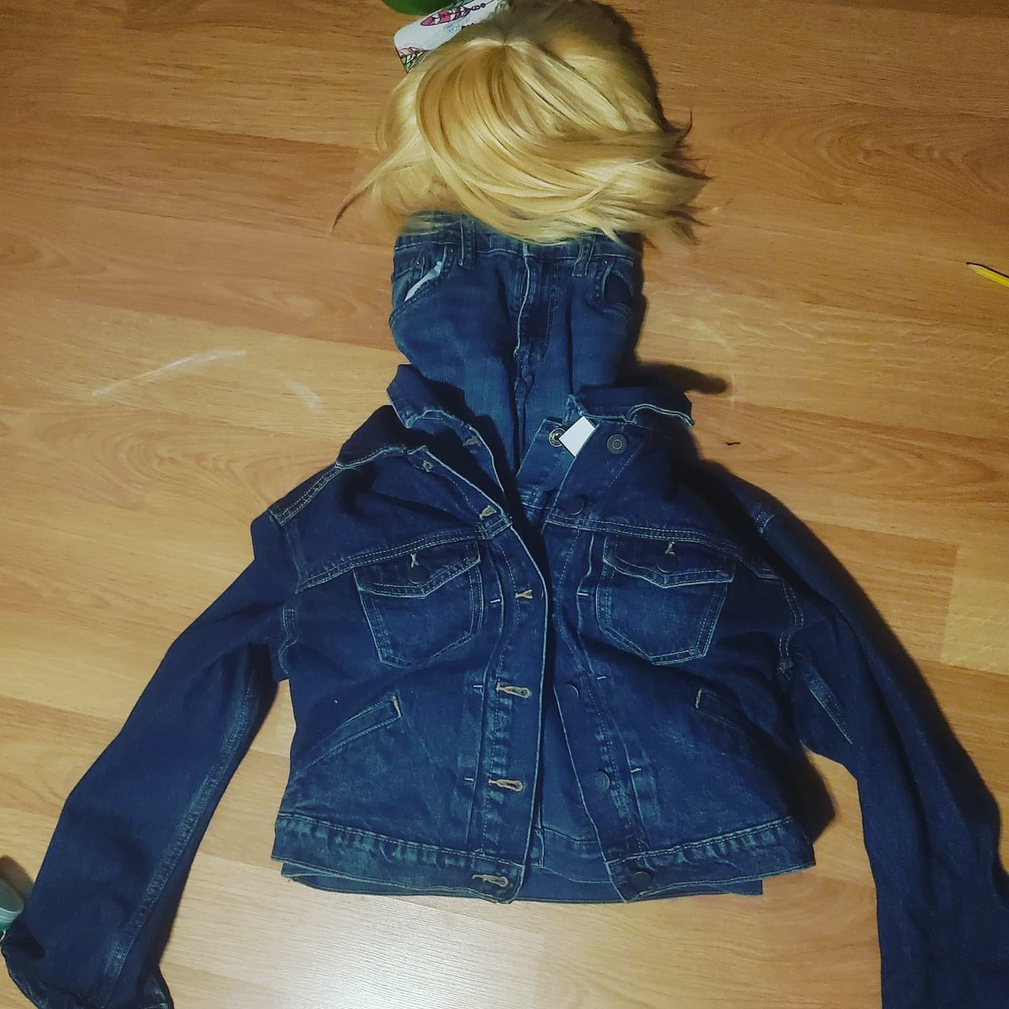 Thrifted jean jackets and small children's jeans arranged on the floor in the shape of a torso and neck, topped by a blond wig