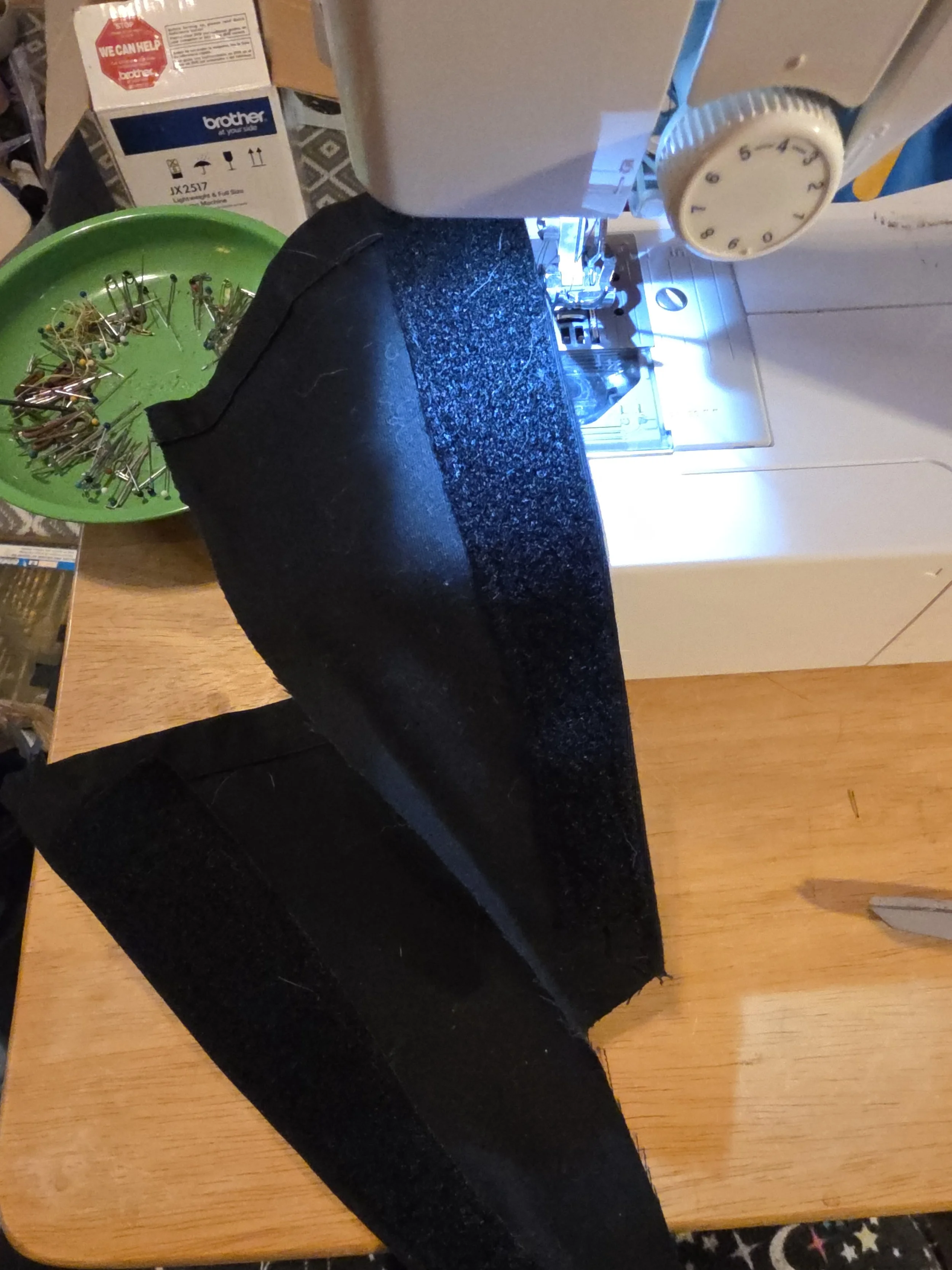 Two triangles of black fabric, one of which is sitting on a sewing machine, showing that a wide strip of velcro has been stitched onto the edge.