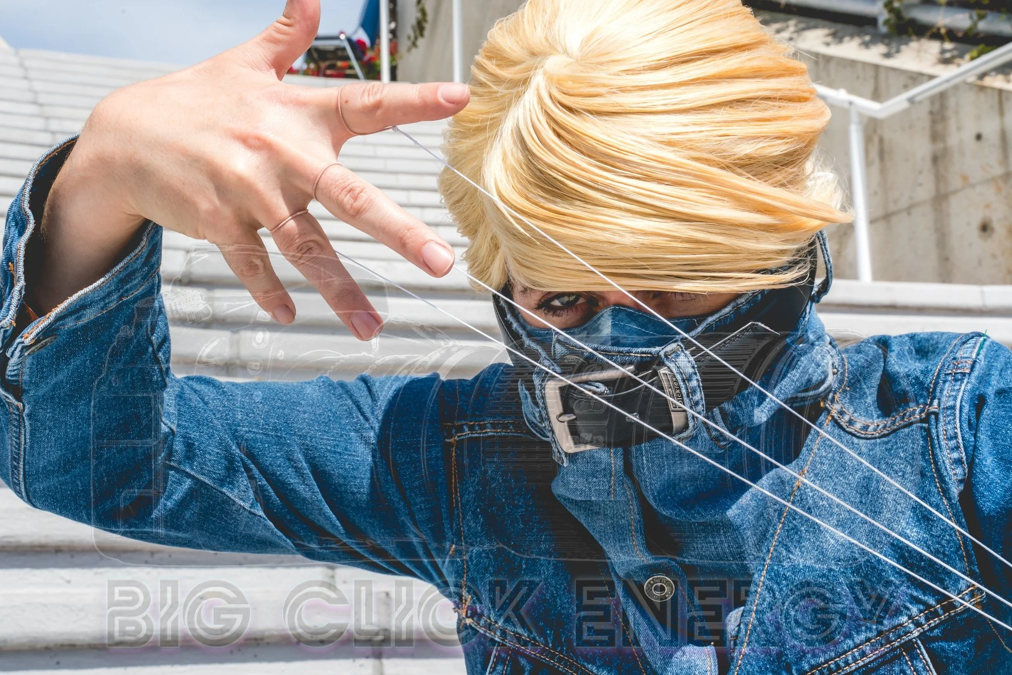 Best Jeanist cosplay from My Hero Academia, wearing a jean jacket with a collar made of the top of another pair of jeans. A smoothly combed blond wig almost covers both eyes, and string extends from the fingers to the other jacket cuff
