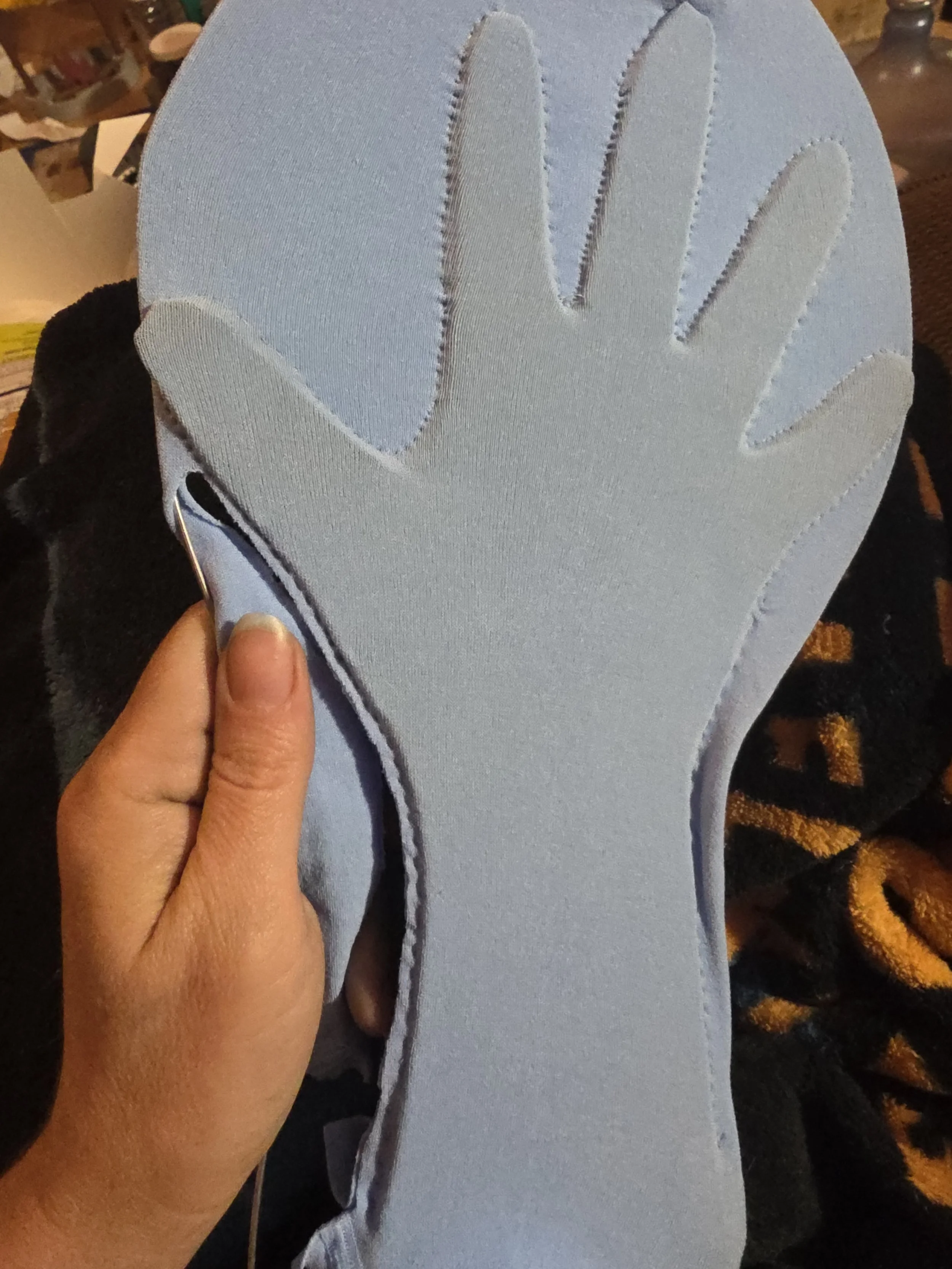 blue tights stretched over a wire hoop surrounding a cardboard hand cutout. The tights are stitched around the cardboard to make a glove. Part of the glove is cut out, freeing it from the wire frame