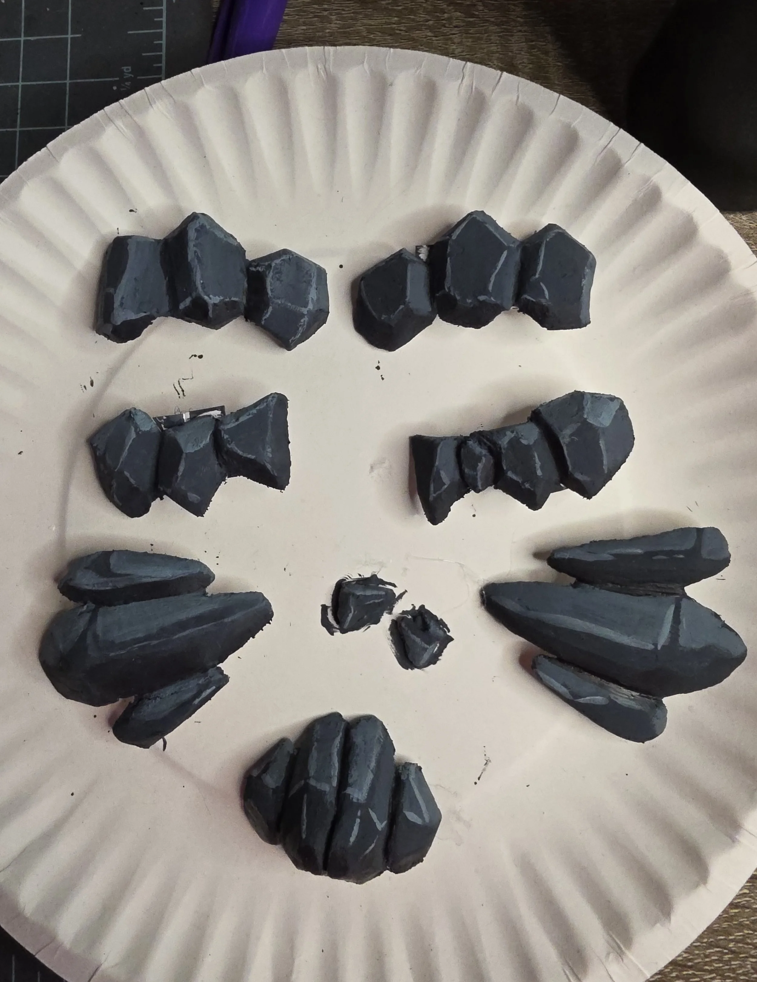 paper plate with worbla rocks arranged on it. Rocks are painted dark bluish gray with some lighter shading
