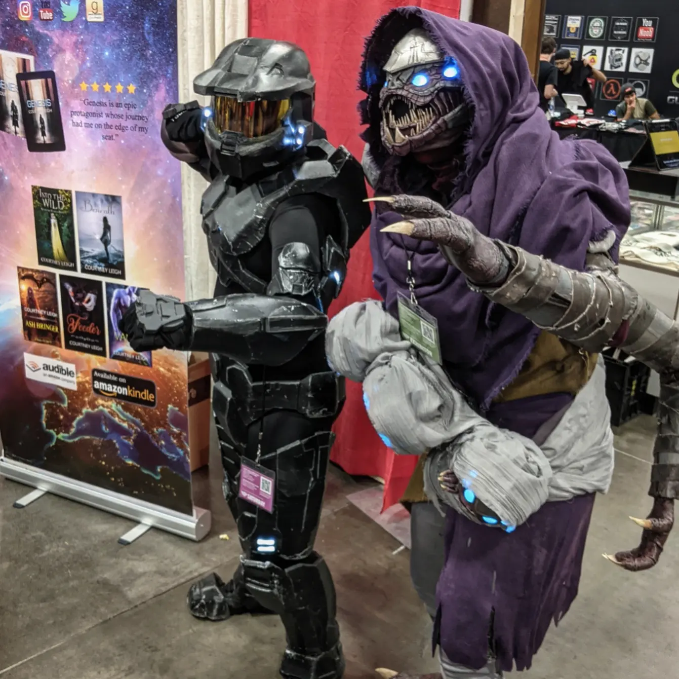 Cosplay of a Buglike alien in a purple hood with 4 glowing blue eyes, 2 claws on each hand, and 2 rows of needle-like teeth. It has 4 swaddled babies of the same species in carried in a baby sling, and stands beside a Halo cosplayer