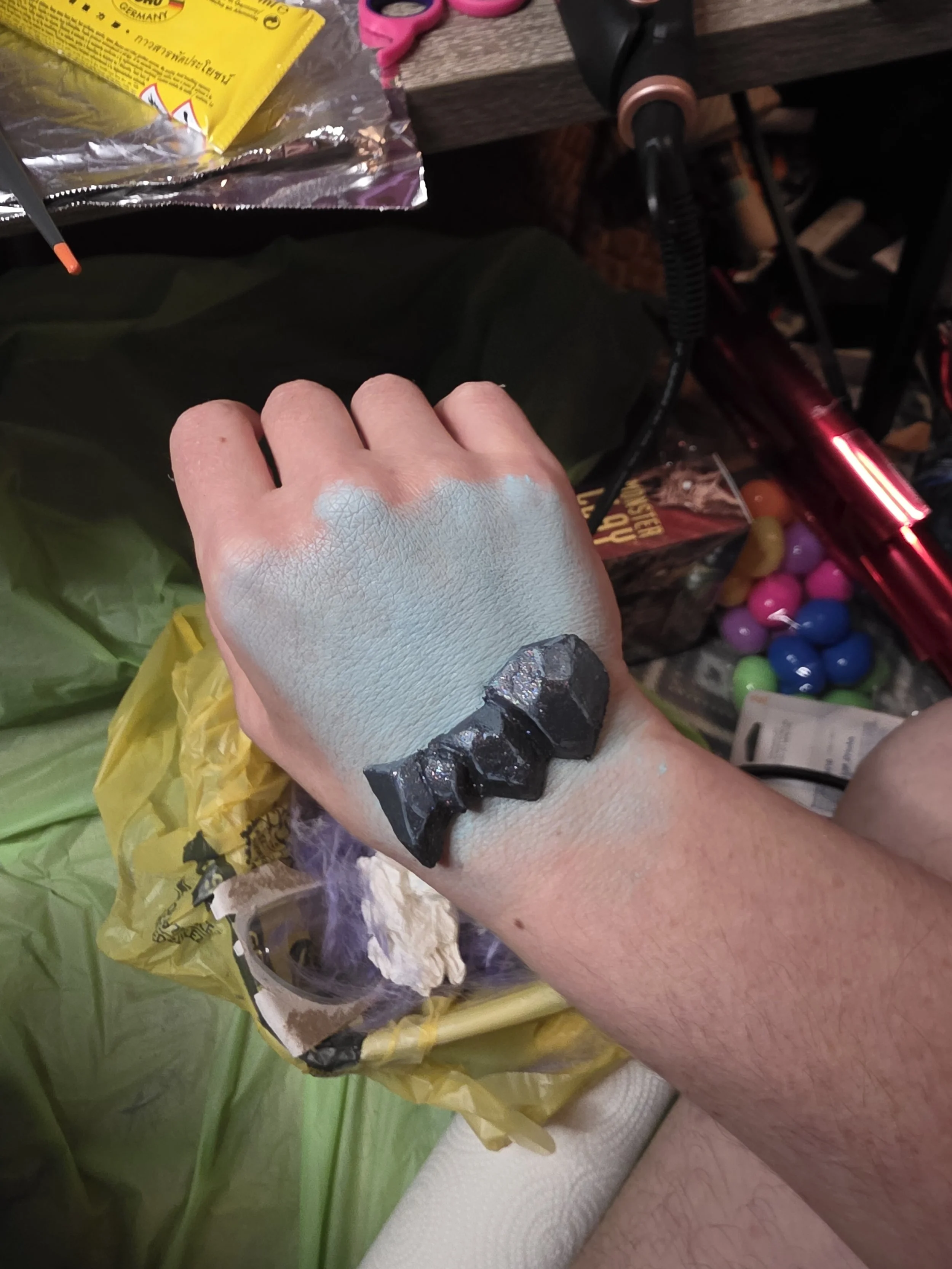 hand with pale blue makeup swatched on the back, and dark blue-gray rocklike scales placed on the wrist
