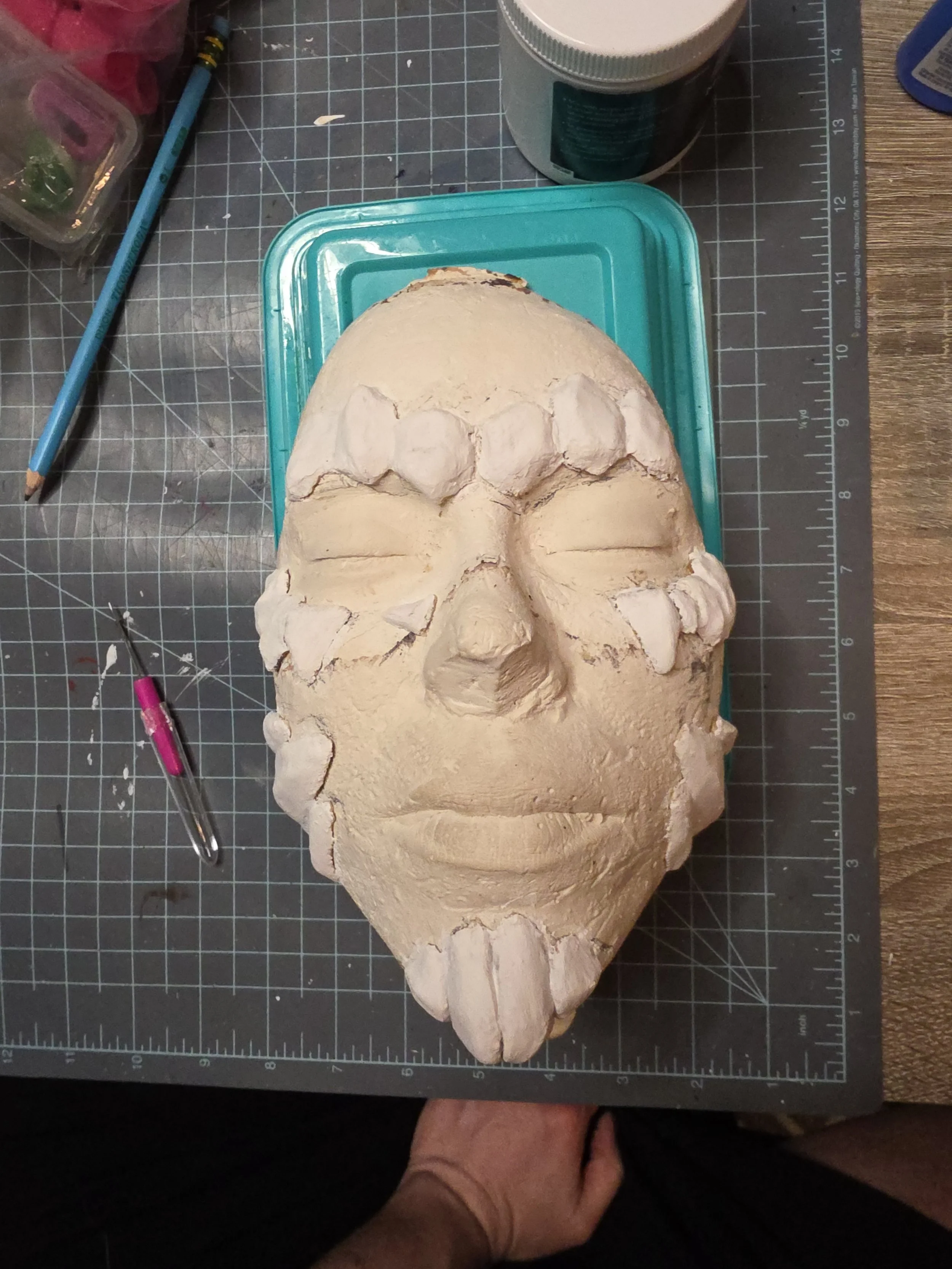 plaster face cast with rocklike scales made of worbla and smoothed with white gesso, placed over the eyebrows, cheekbones, chin, and jawline
