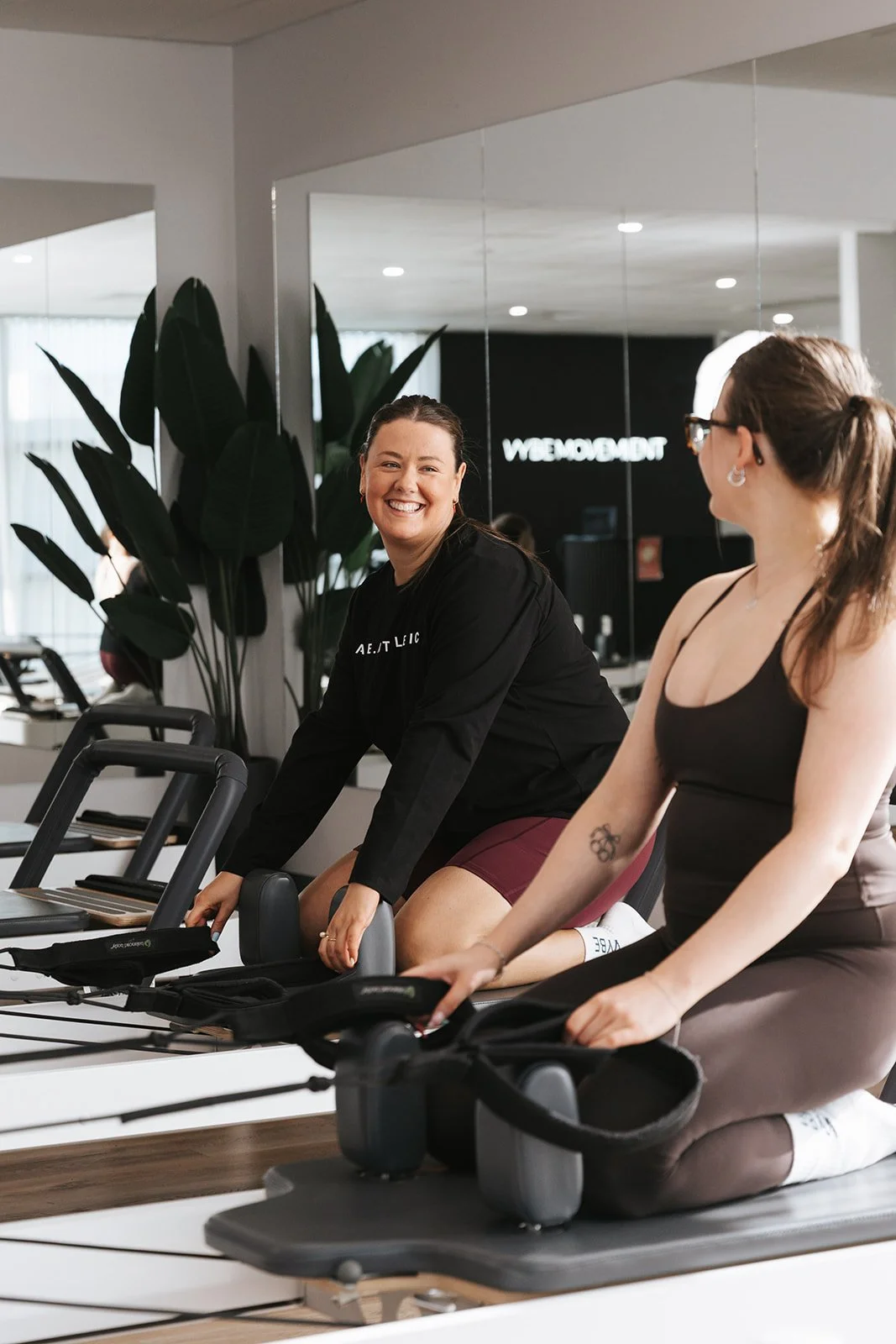 Two trainers engaging and chatting on the reformer machine at Vybe Movement.