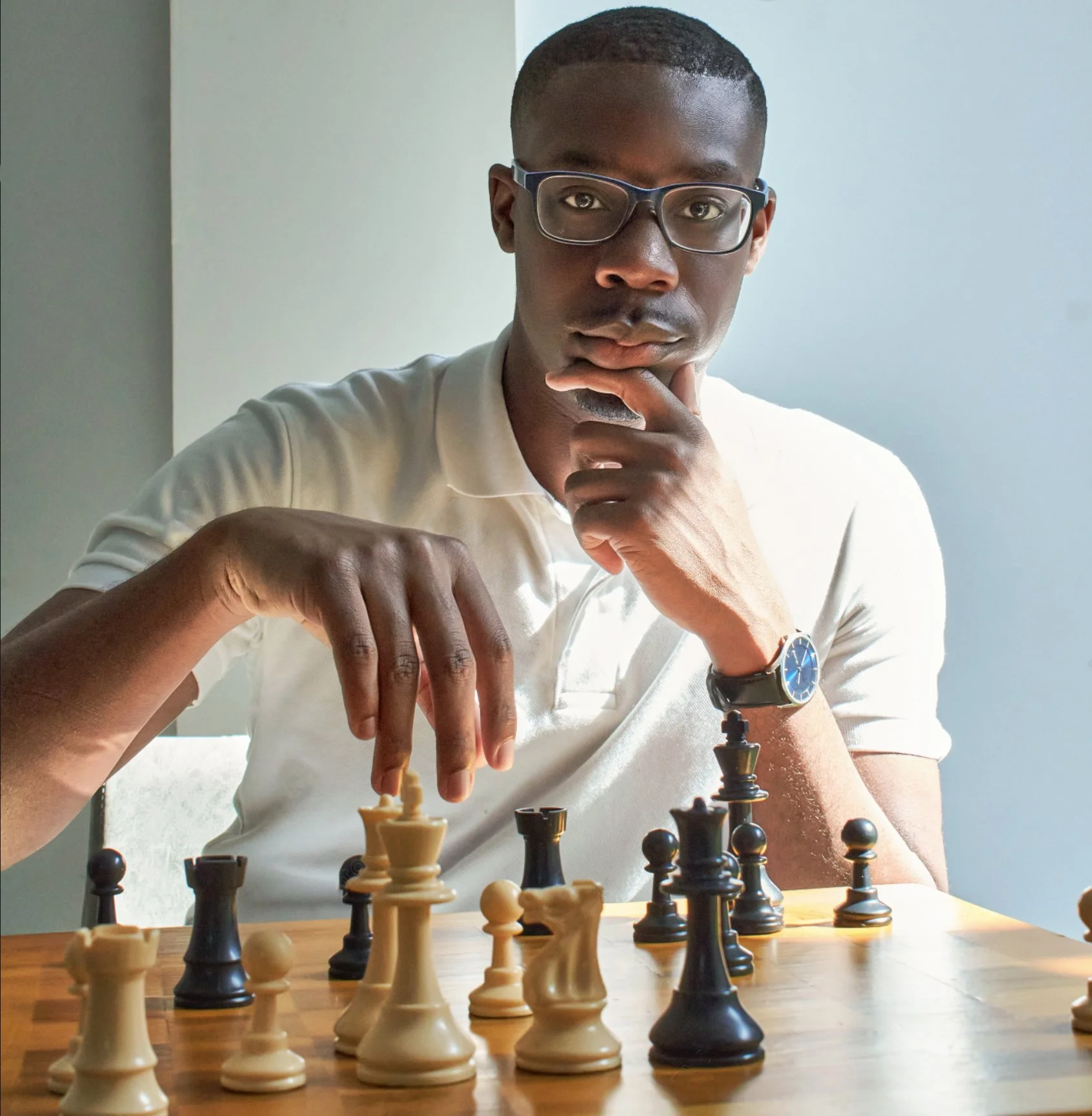 A man with glasses and a watch plays chess at a table.