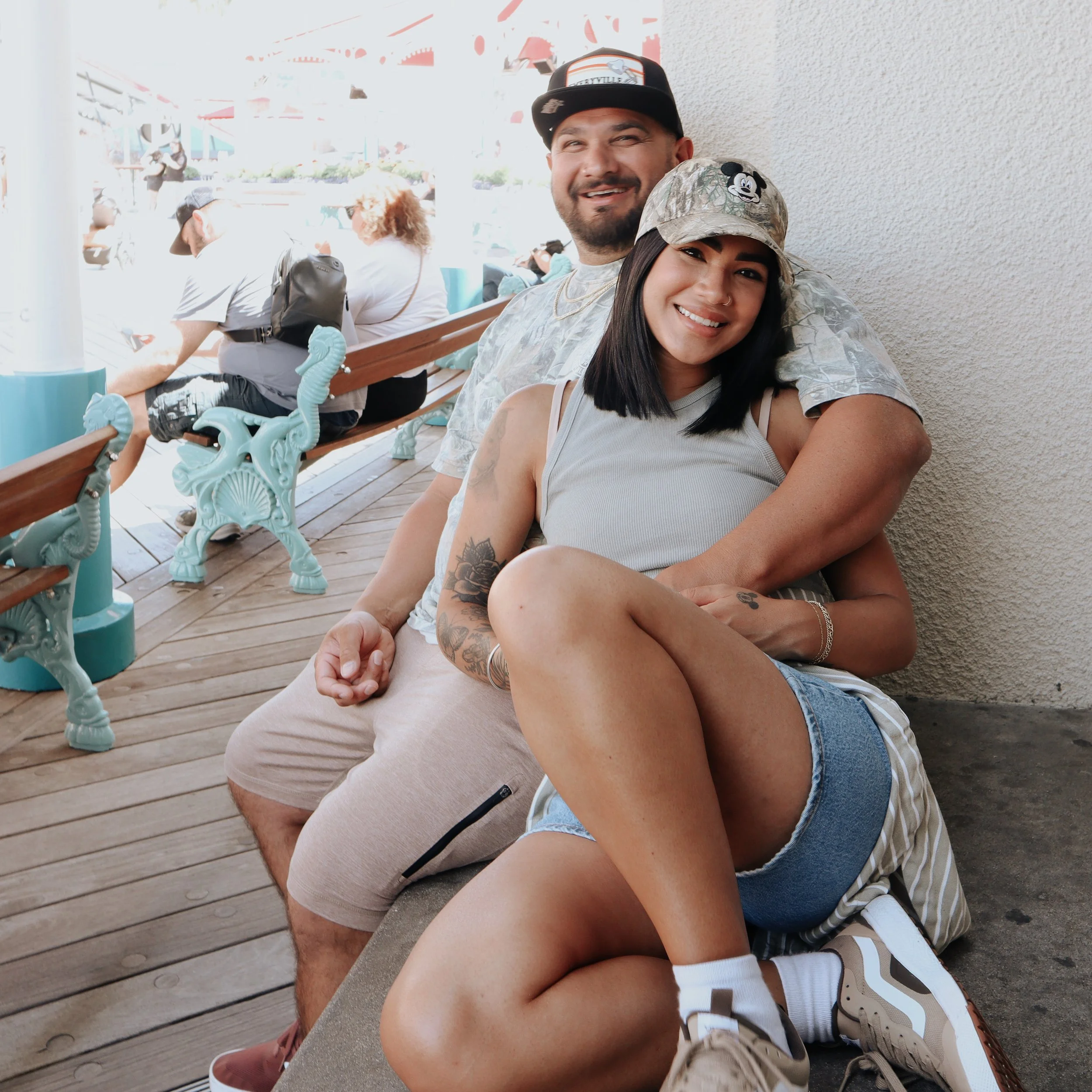 Husband and wife on bench at an amusement park, with other park visitors in the background.