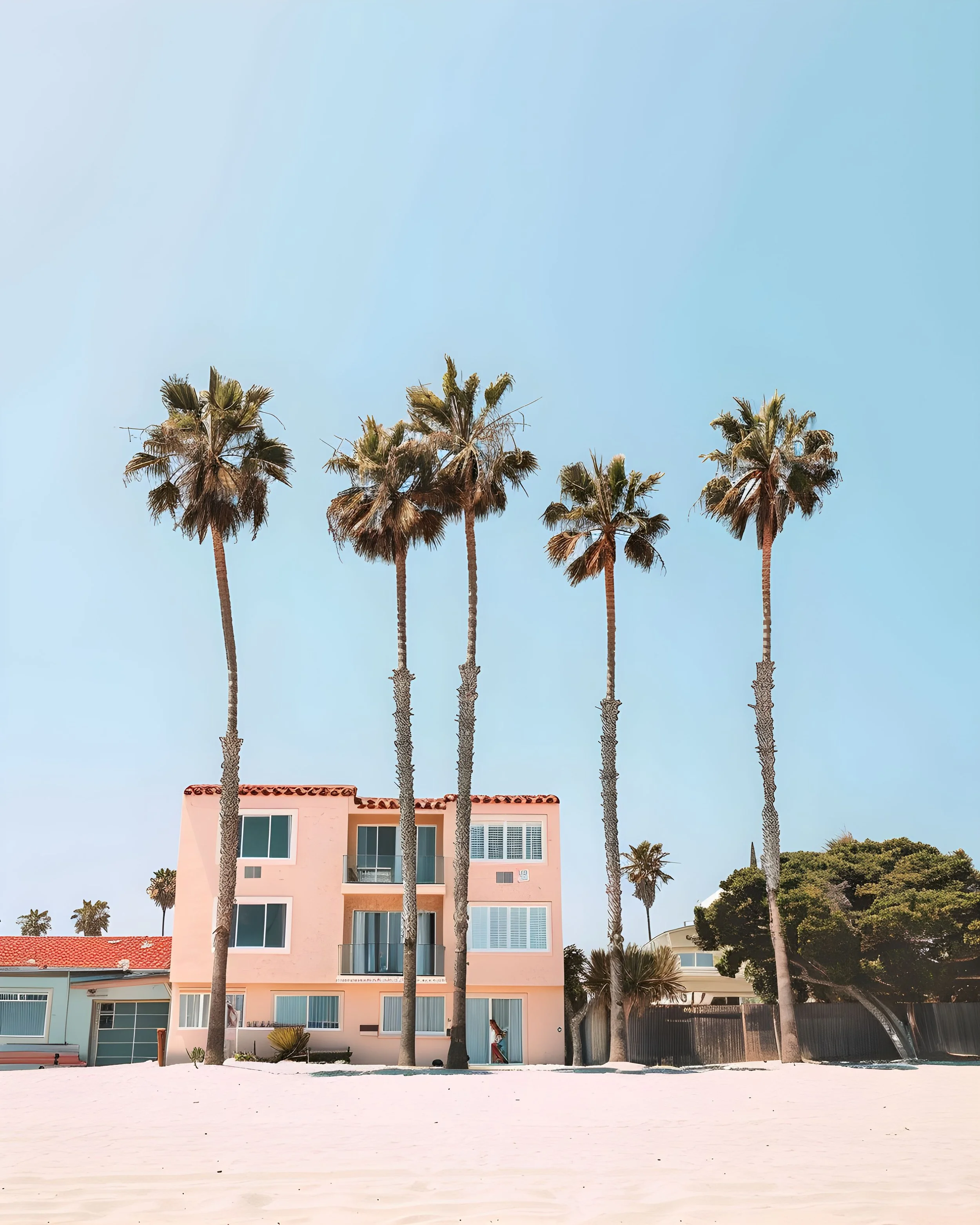 A pink beach house with palm trees in front, set against a clear blue sky.