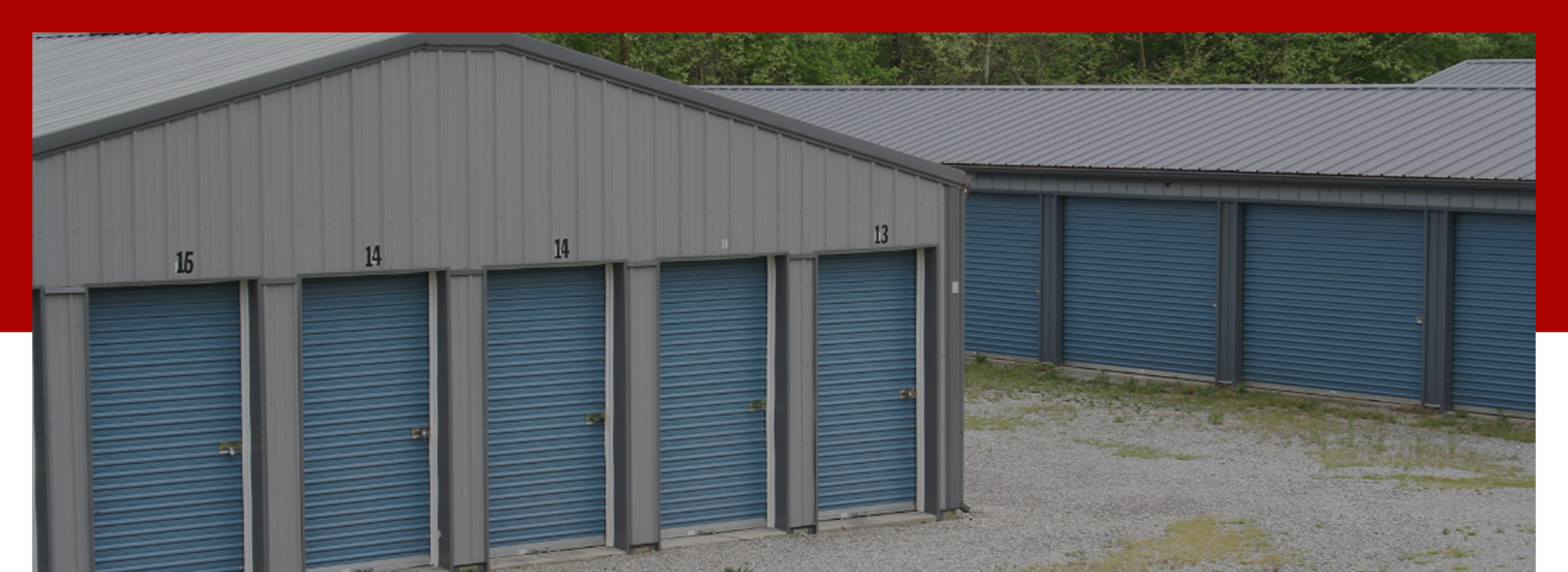 A row of storage units with blue roll-up doors, numbered 15, 14, and 13, in a gravel lot with a grassy area and trees in the background.