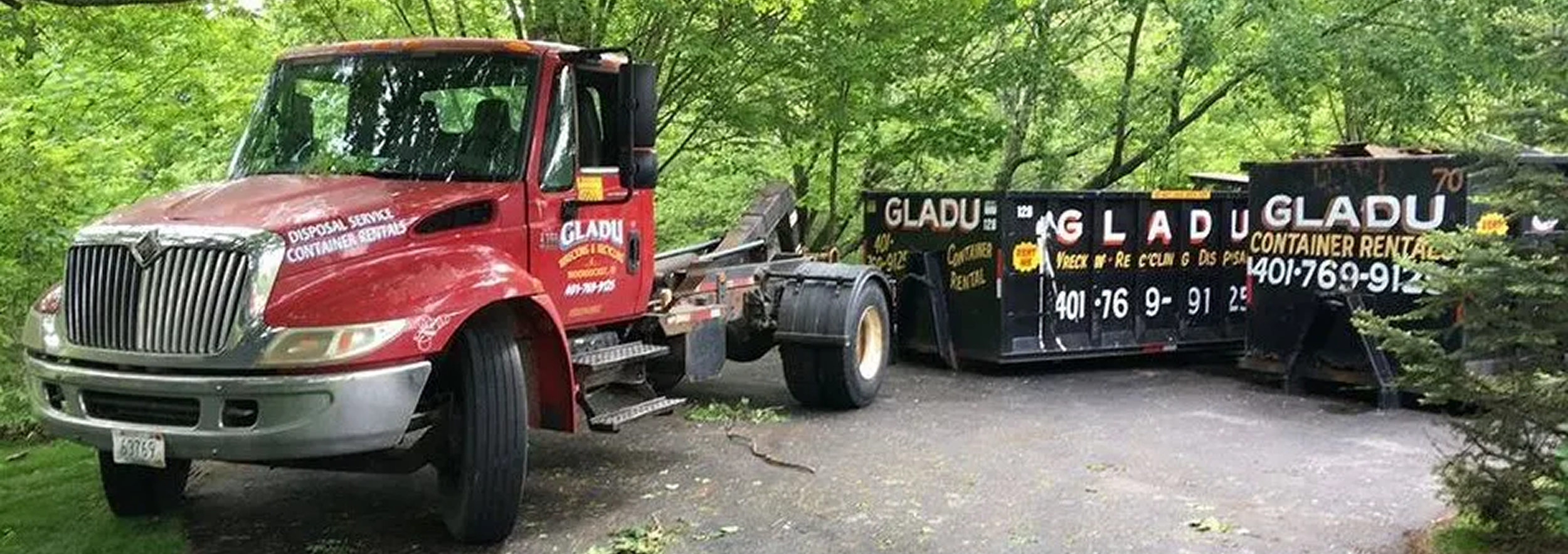 Red truck with black flatbed trailer parked on a wooded area, advertising container rental with a phone number