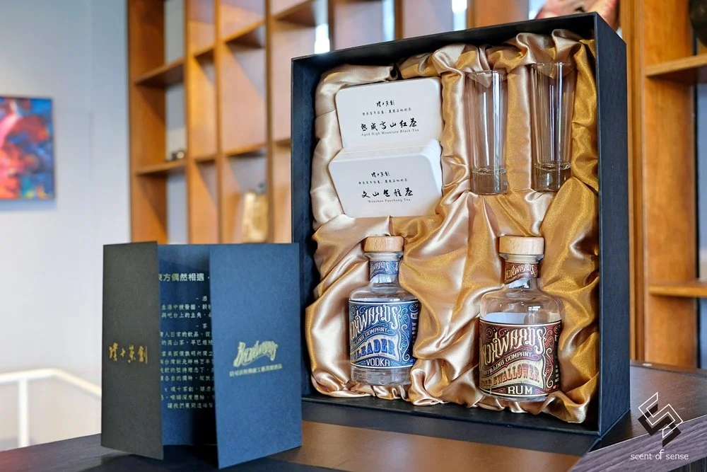 A gift box containing two miniature bottles of alcohol, two small boxes, and two small glasses, all arranged on a satin lining.