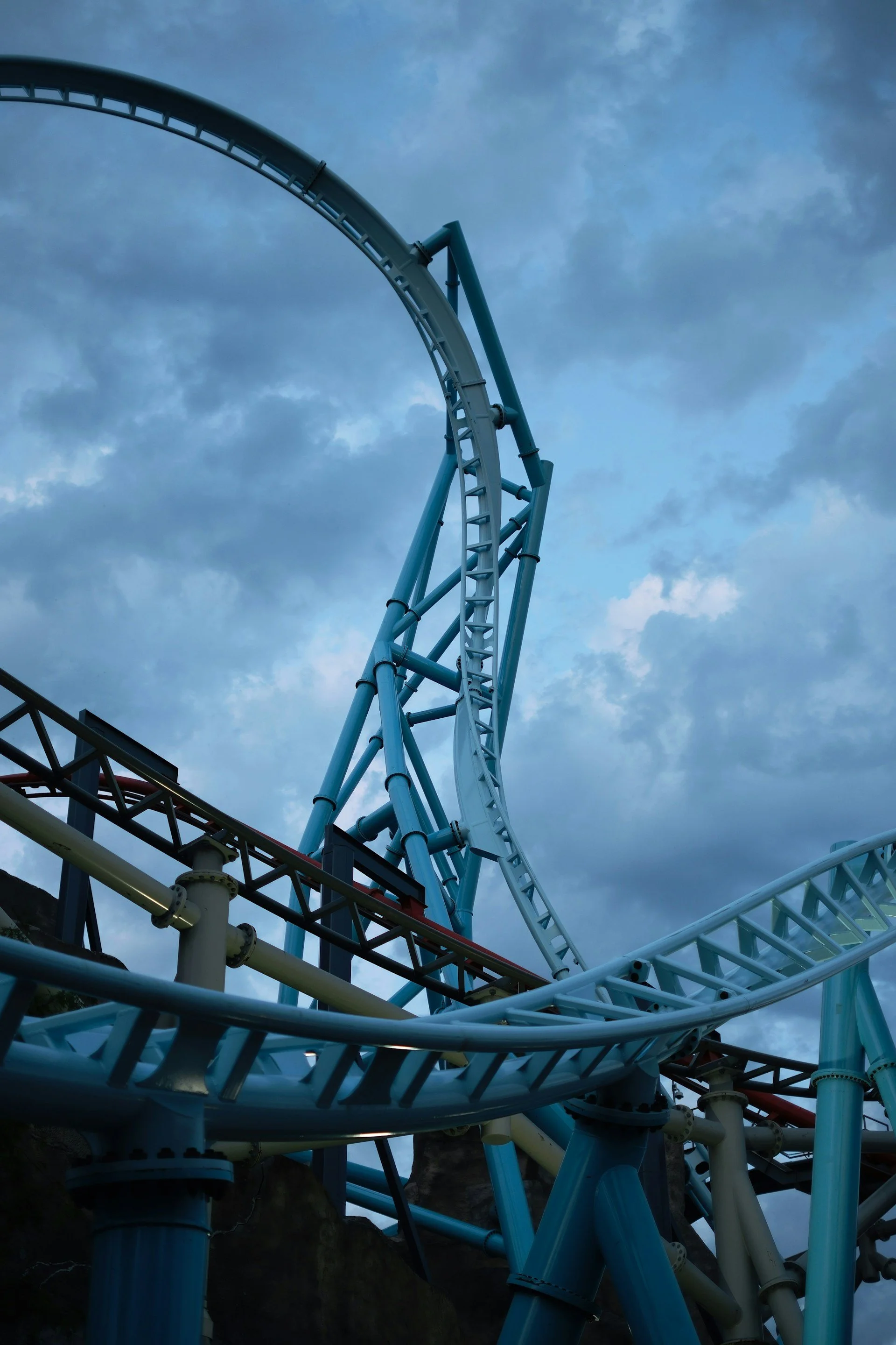 Close-up view of a roller coaster track with a steep drop and sharp turns against a cloudy sky.