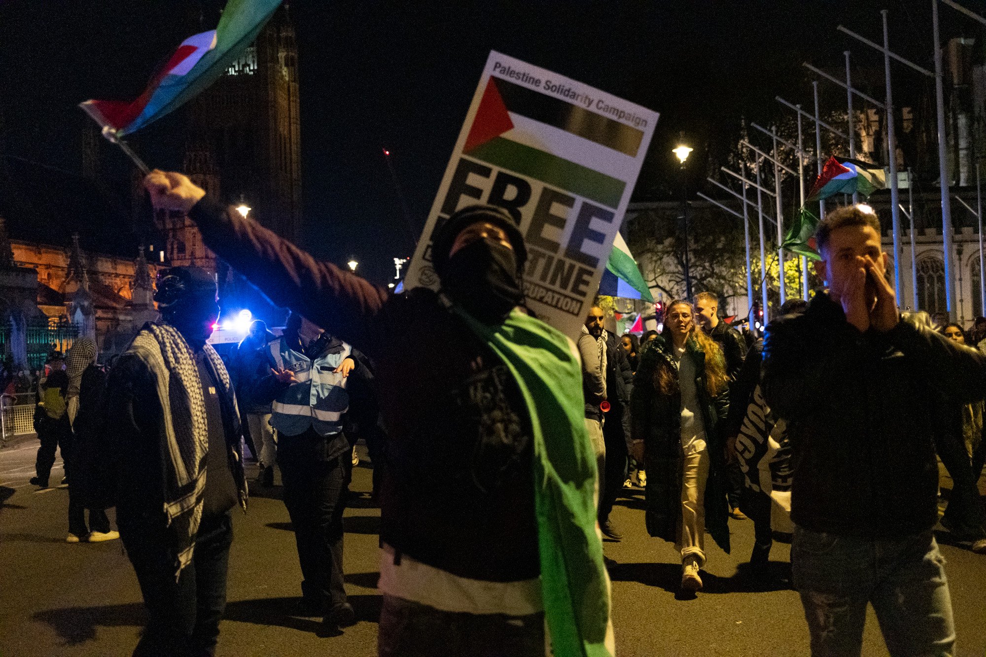 A protester wearing and waving Palestine flags leads a march away from the Houses of Parliament through London - November 15, 2023