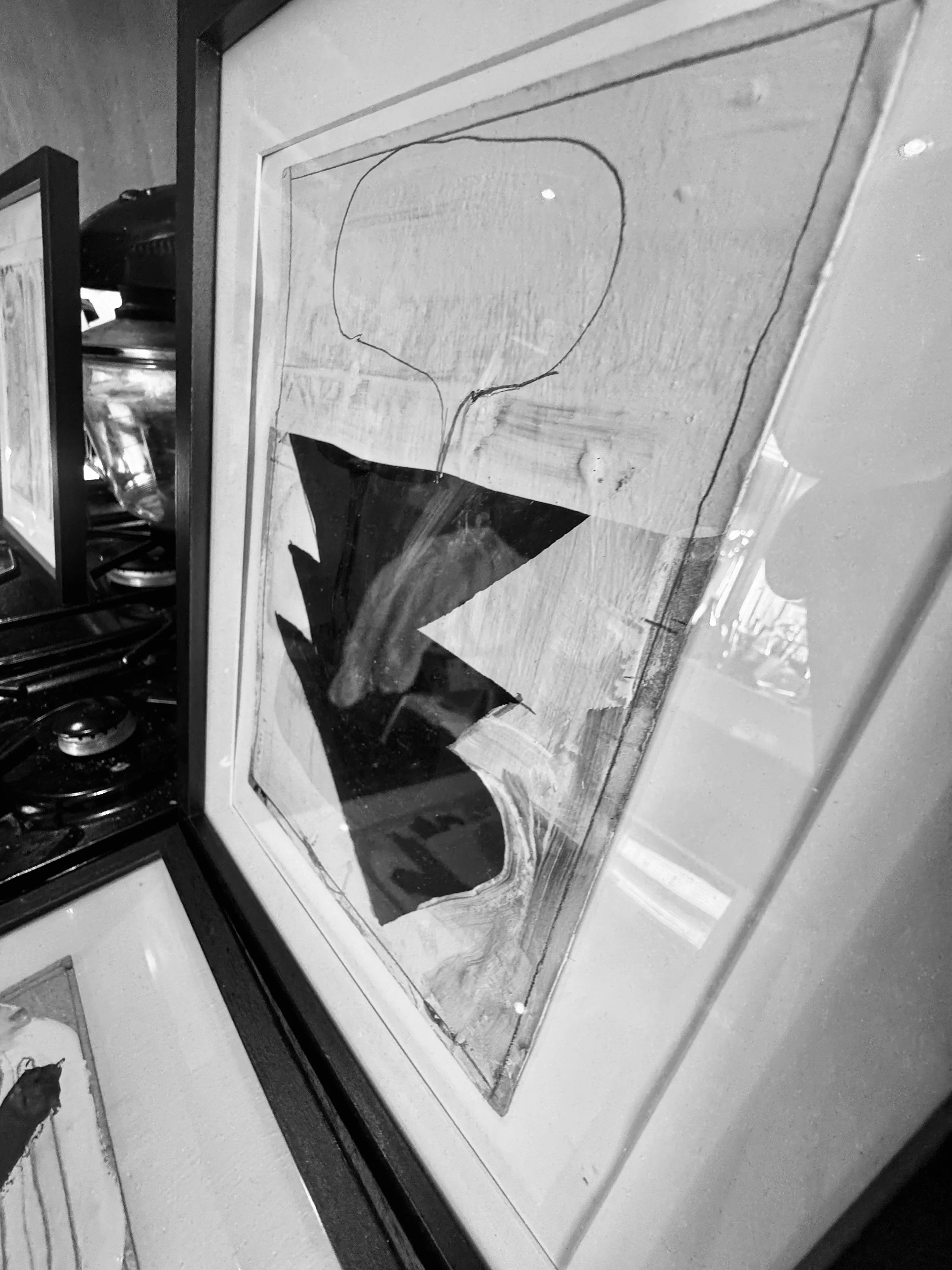 A framed abstract artwork with a large black zigzag shape and a speech bubble outline on a wooden background, leaning against a wall among other framed pieces.