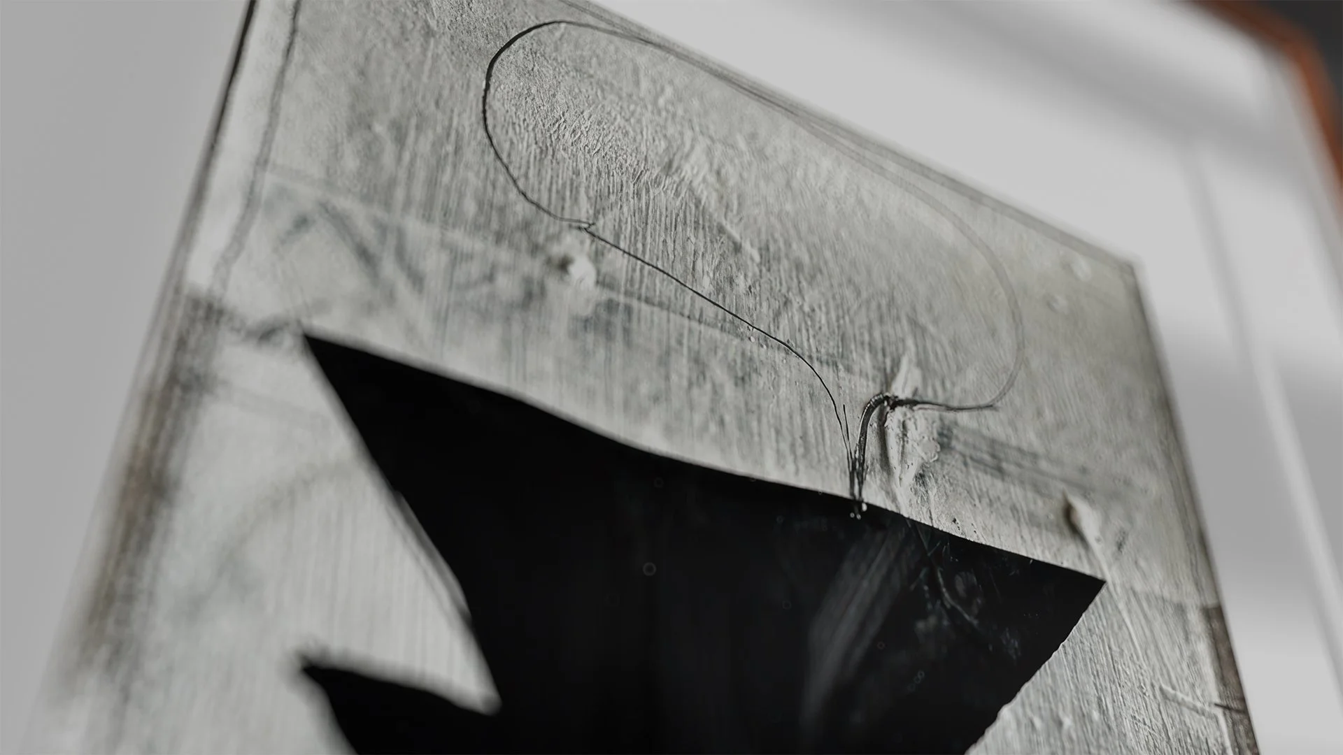 Close-up of a white textured surface with a black geometric shape and thin black lines drawing on it.
