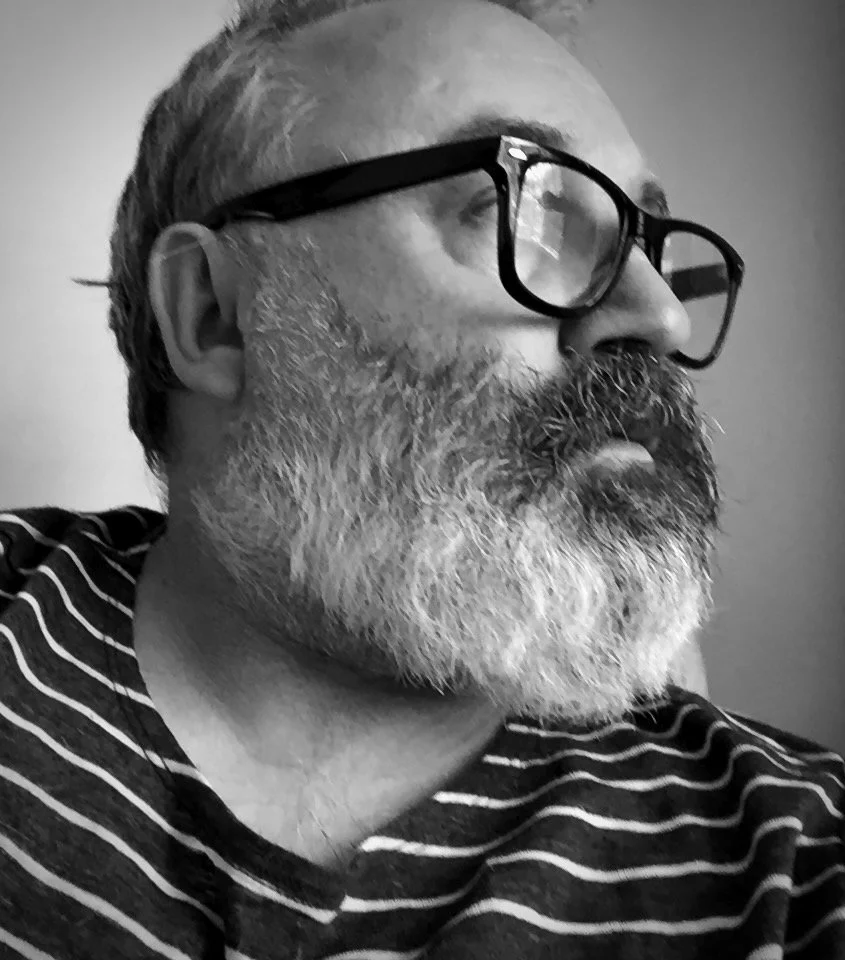 A black and white side profile of a man with glasses, a beard, and wearing a striped shirt.