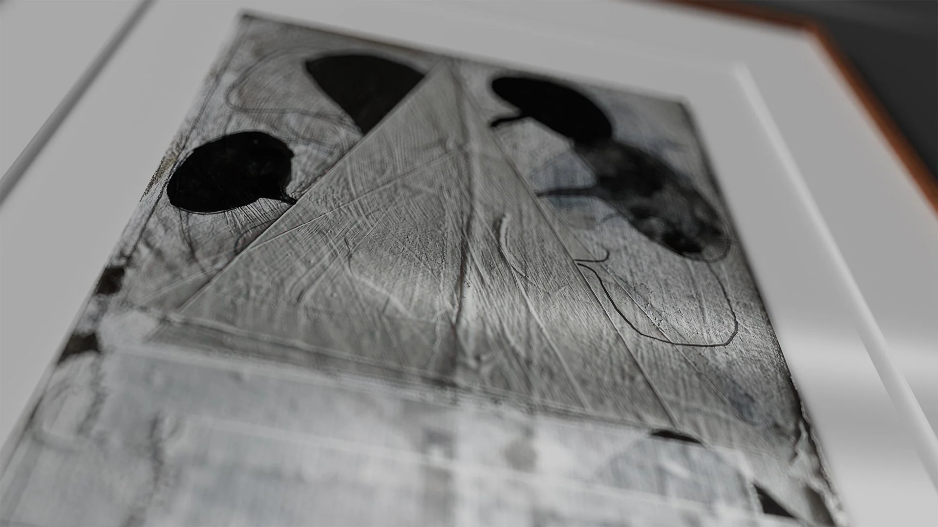 Close-up photograph of a shattered photograph or artwork featuring black silhouettes of balloons or similar objects on a textured, cracked surface.