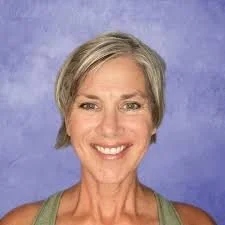 Portrait of a smiling woman with short gray hair against a blue background.