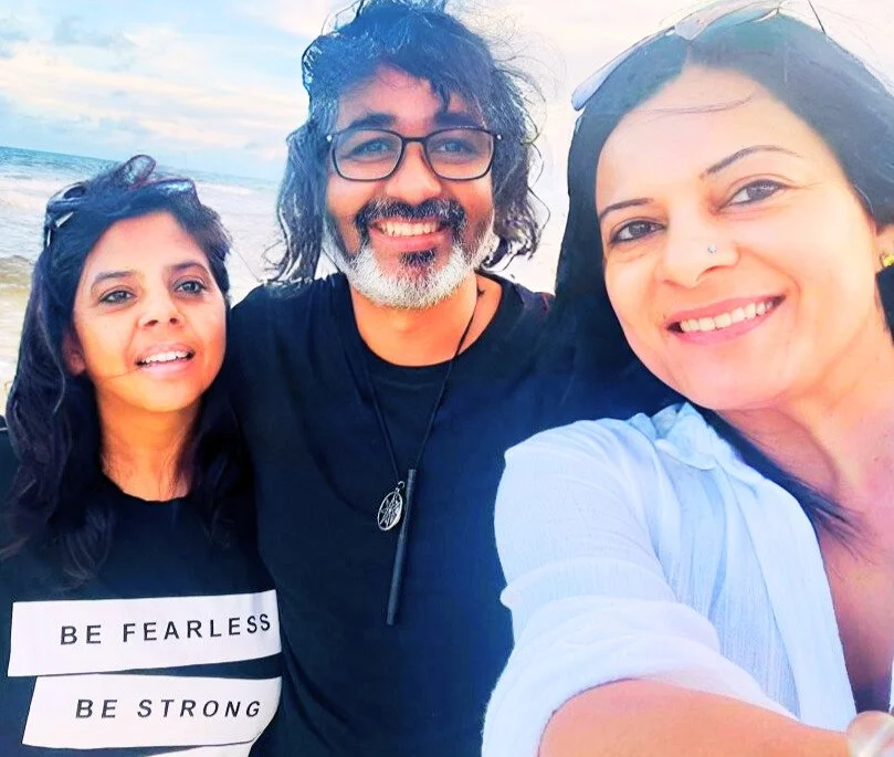 Three people, two women and one man, smiling and taking a selfie at the beach with waves in the background.