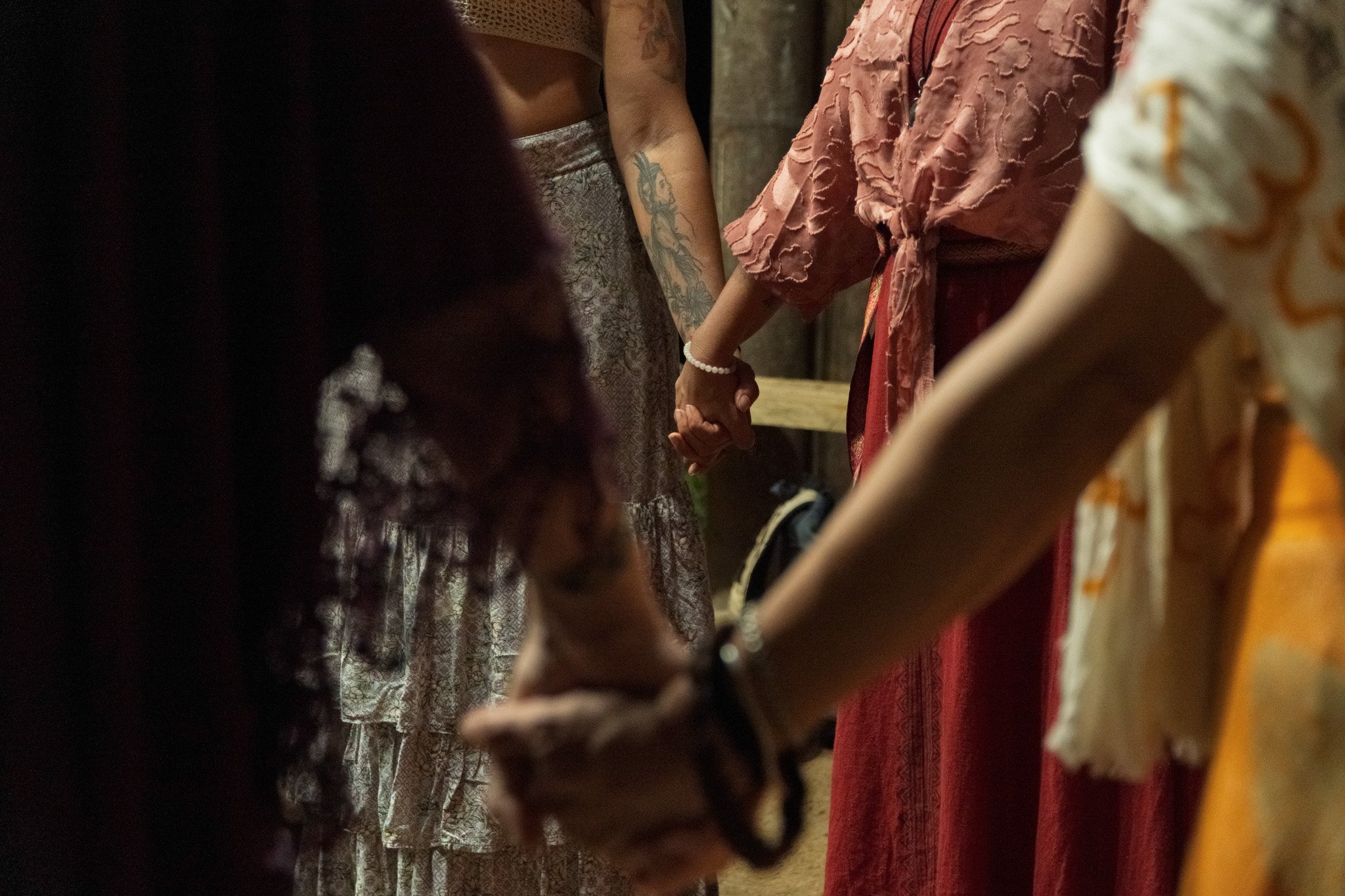 Group of five women sitting outdoors with a blue sky and trees in the background, smiling and enjoying wine.