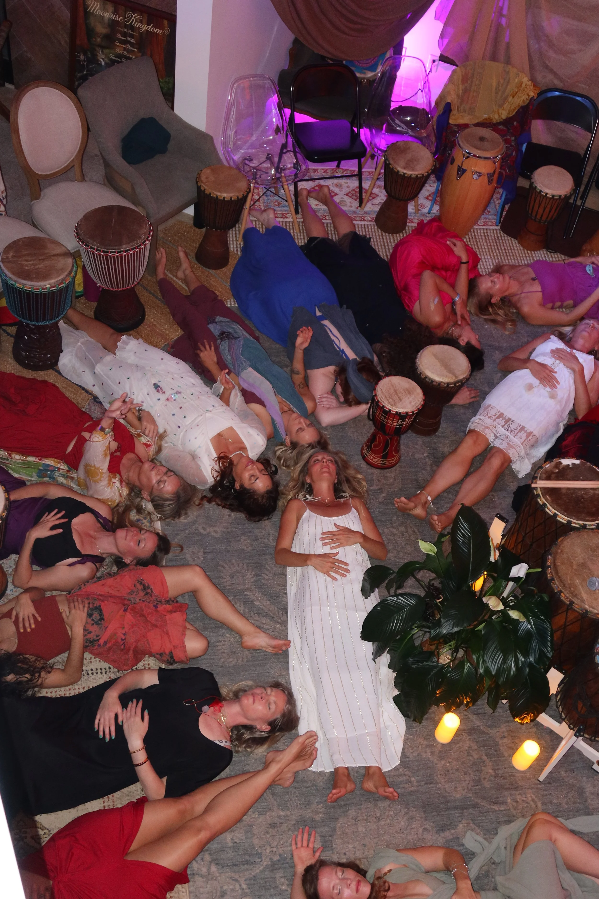 A table decorated with two small statues of meditating children, several wine glasses, metallic bowls, candles, and various utensils, set against a mirrored wall reflecting a blue and purple mandala design.