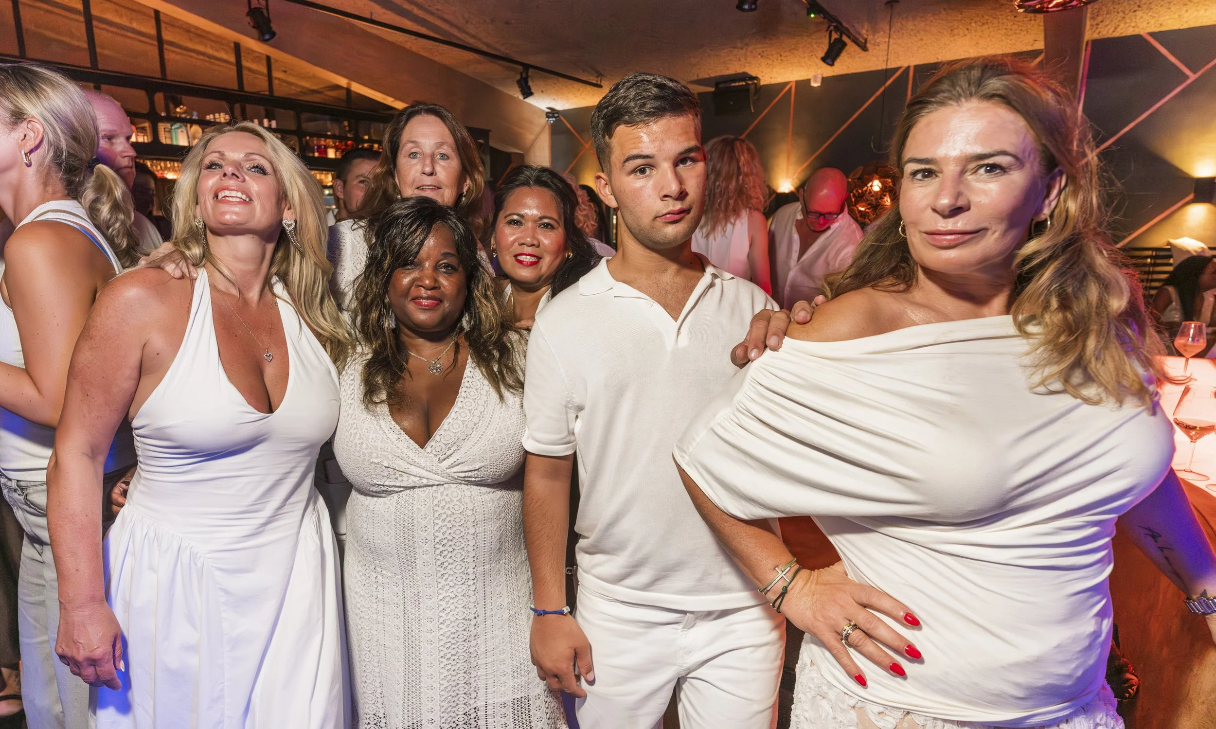 Een groep mensen die samen poseert tijdens een feest of bijeenkomst in een binnenruimte met warme verlichting.