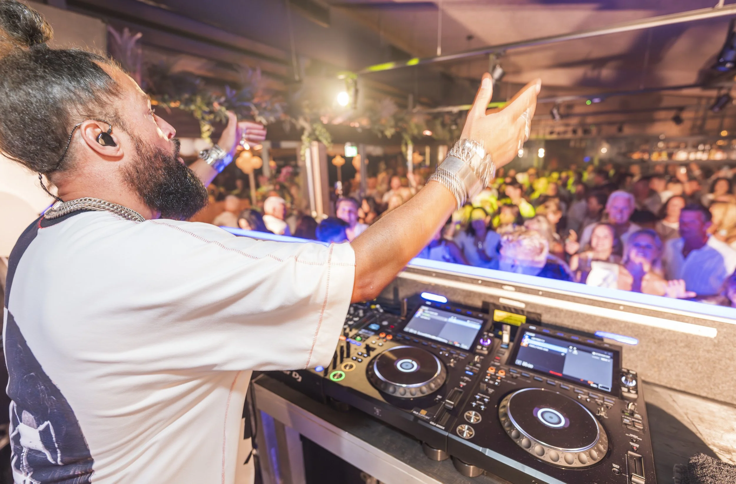 DJ met luidsprekers en mengpaneel die optreedt op een feest met een dansend publiek in een club of evenementenhal.