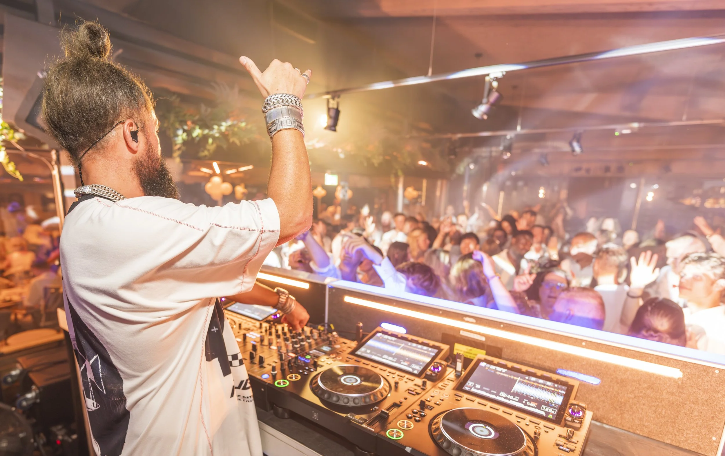 DJ die muziek draait in een club met een menigte mensen die danst onder kleurrijke verlichting.