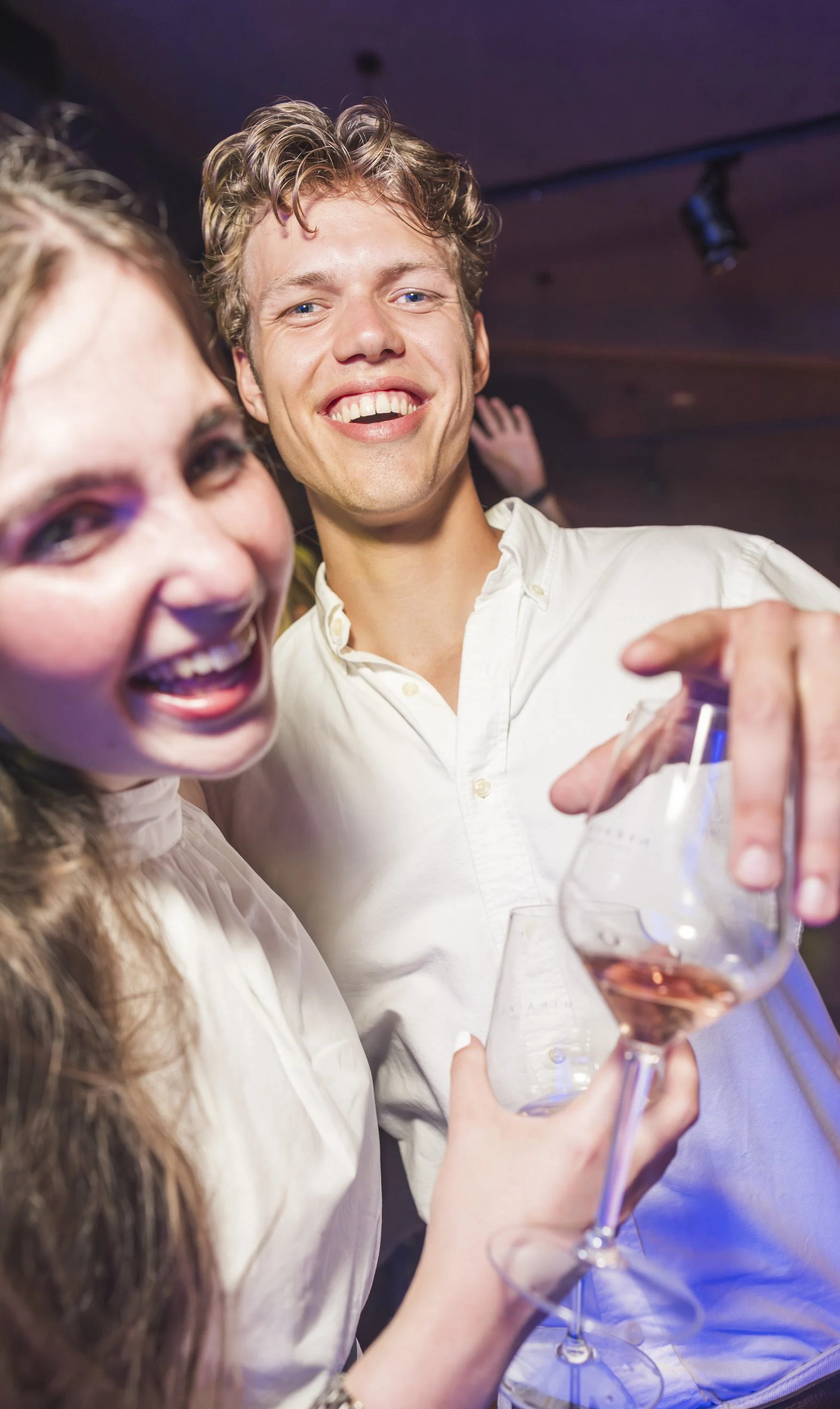 Twee mensen lachen en proeven wijn tijdens een feestje.