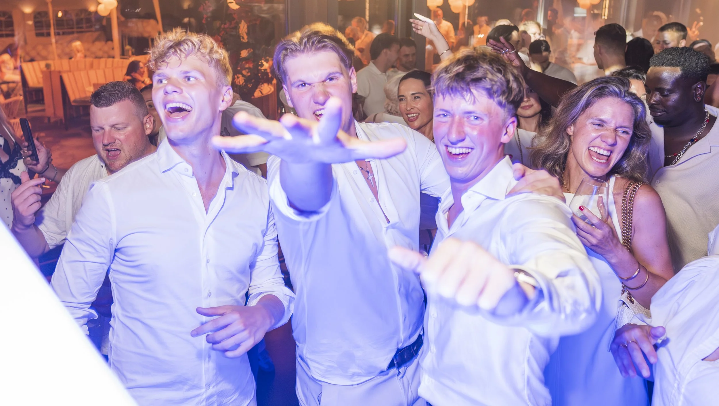Groep mensen die feest vieren en dansen op een feest met kleurrijke verlichting en een gezellige sfeer.
