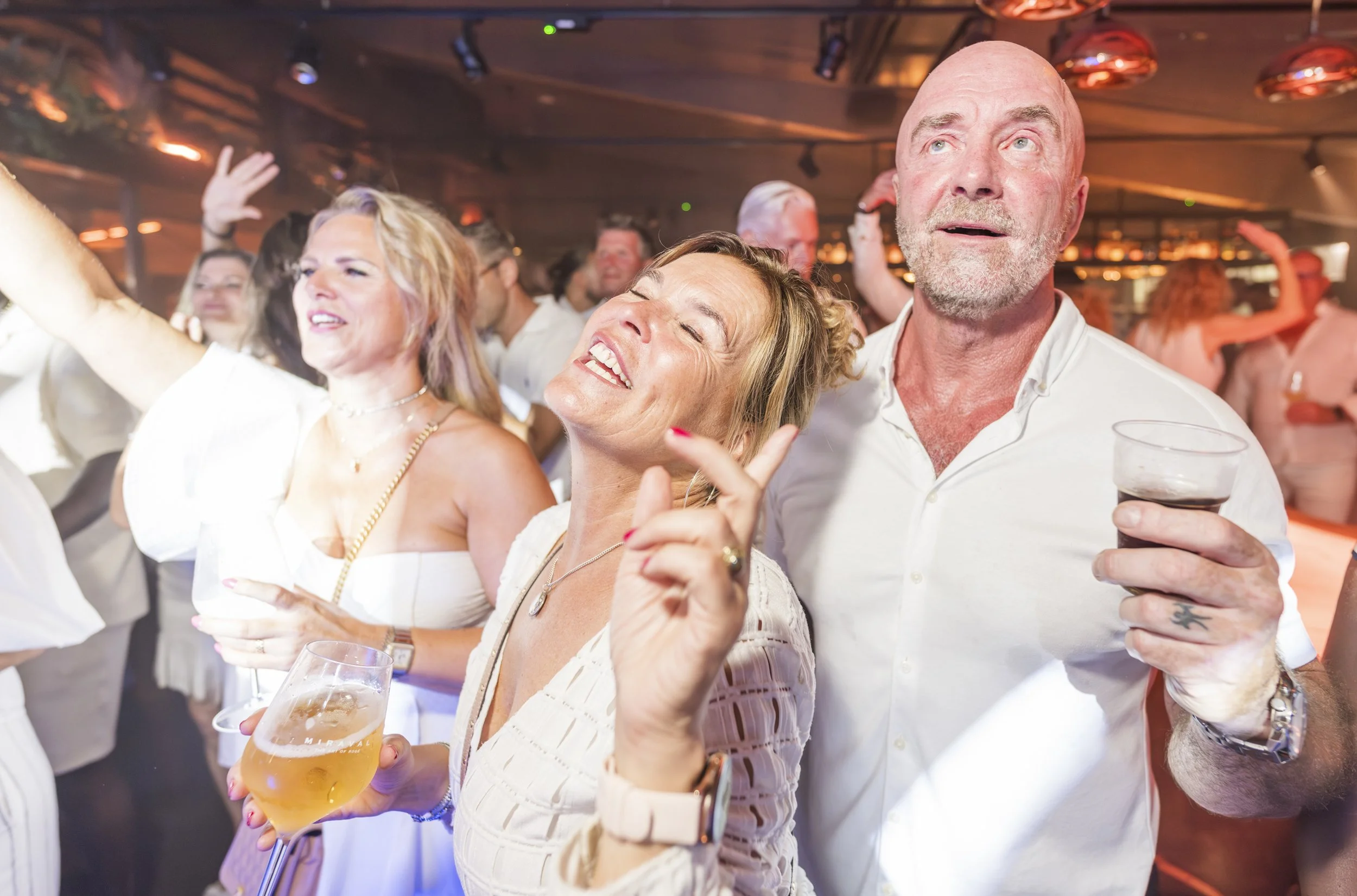 Mensen vieren feest in een bar, lachend en dansend, met glazen bier in de hand.