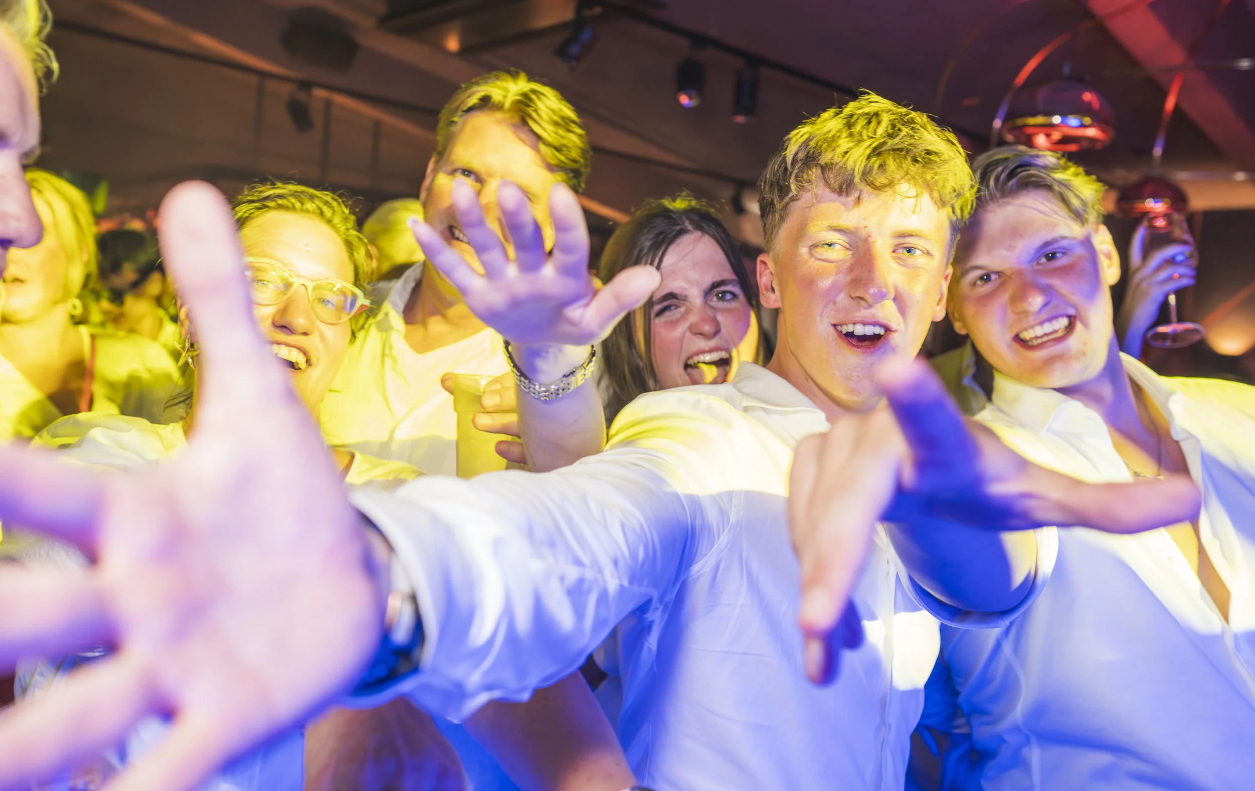 Een groep mensen die plezier maken op een feest of bijeenkomst, lachend en met uitgestrekte armen.