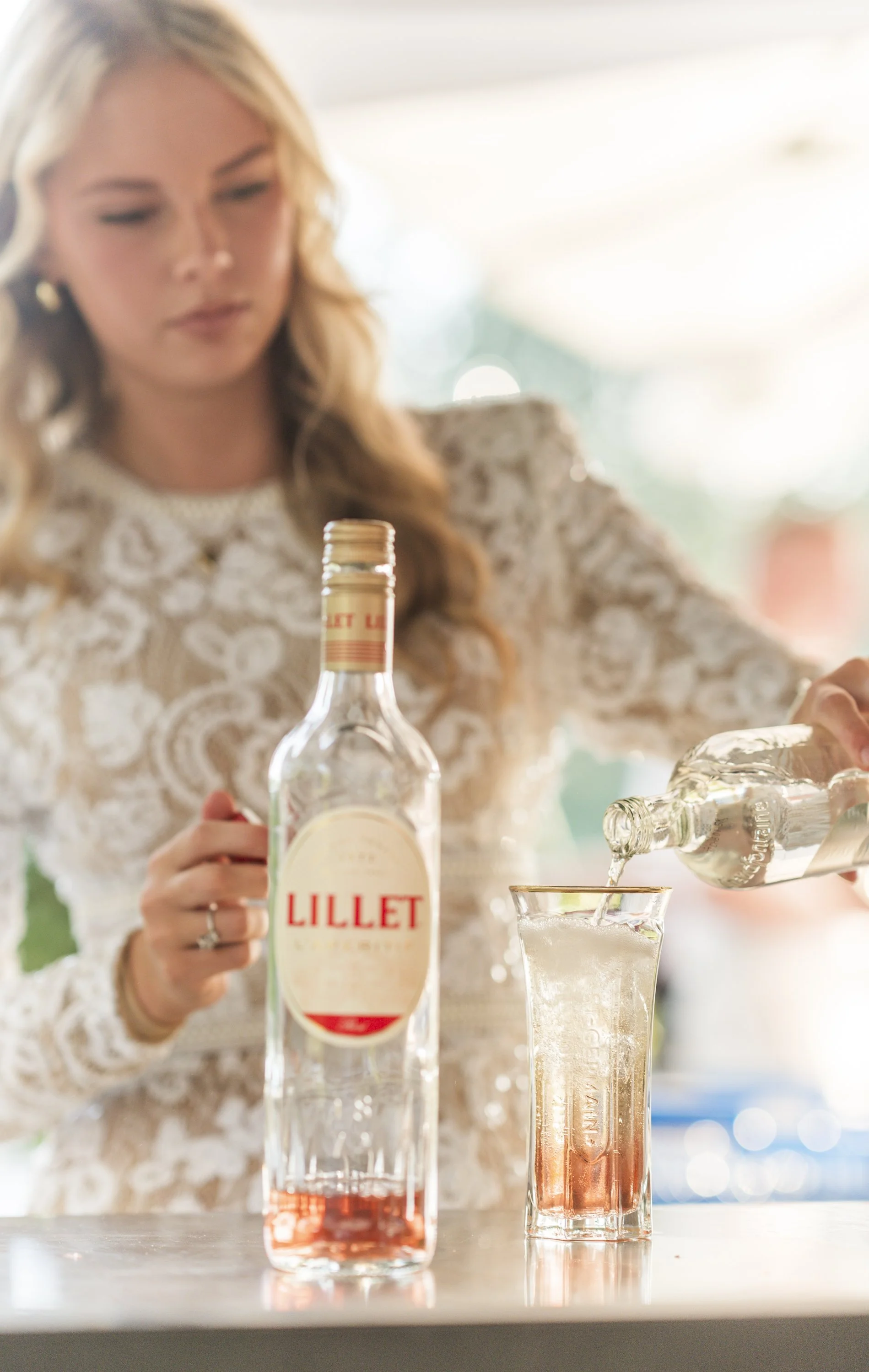 Een vrouw schenkt een drankje uit een fles Lillet in een glas met ijs.