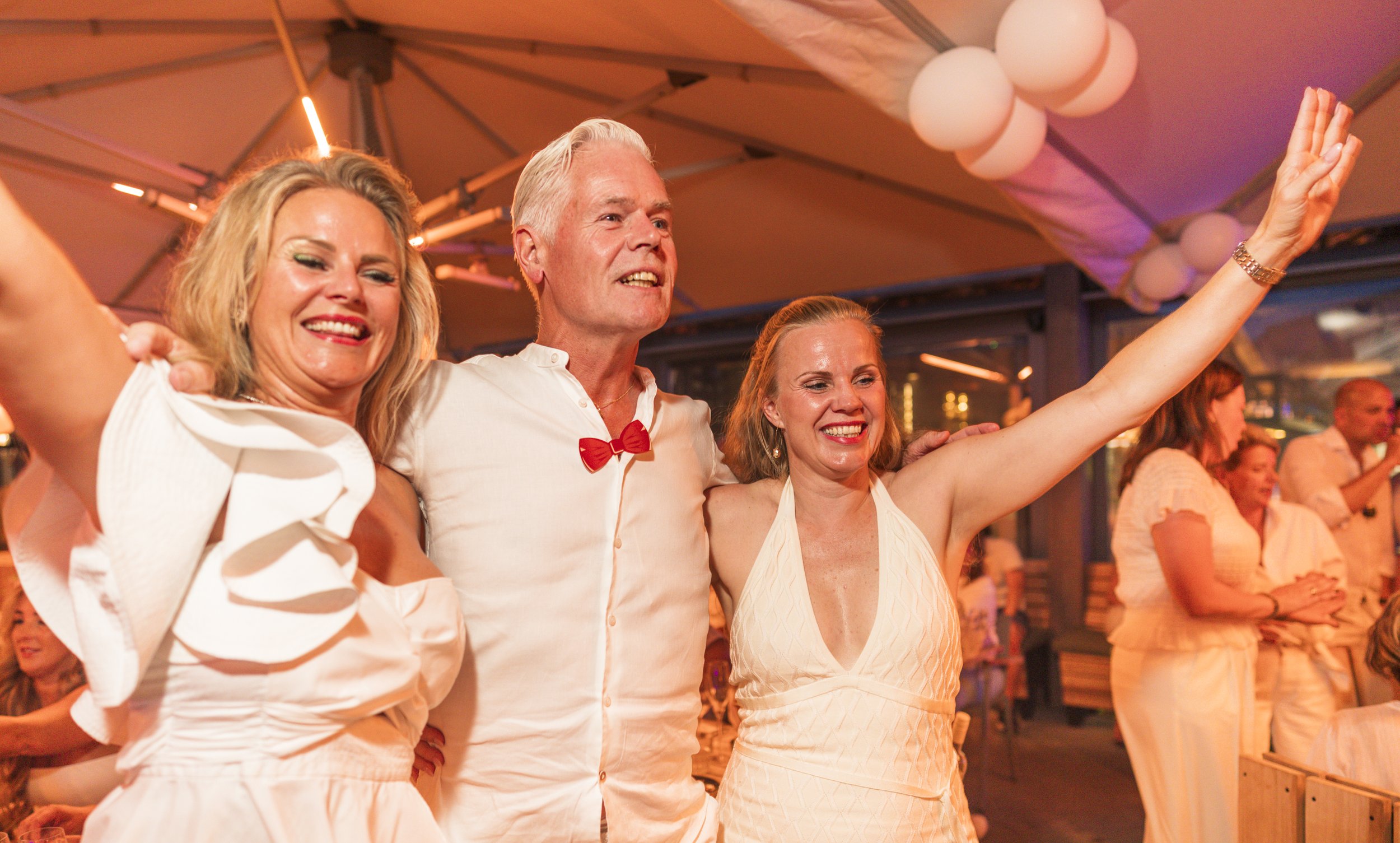 Groep mensen die samen danst en plezier hebben op een feest met warme verlichting en decoraties.
