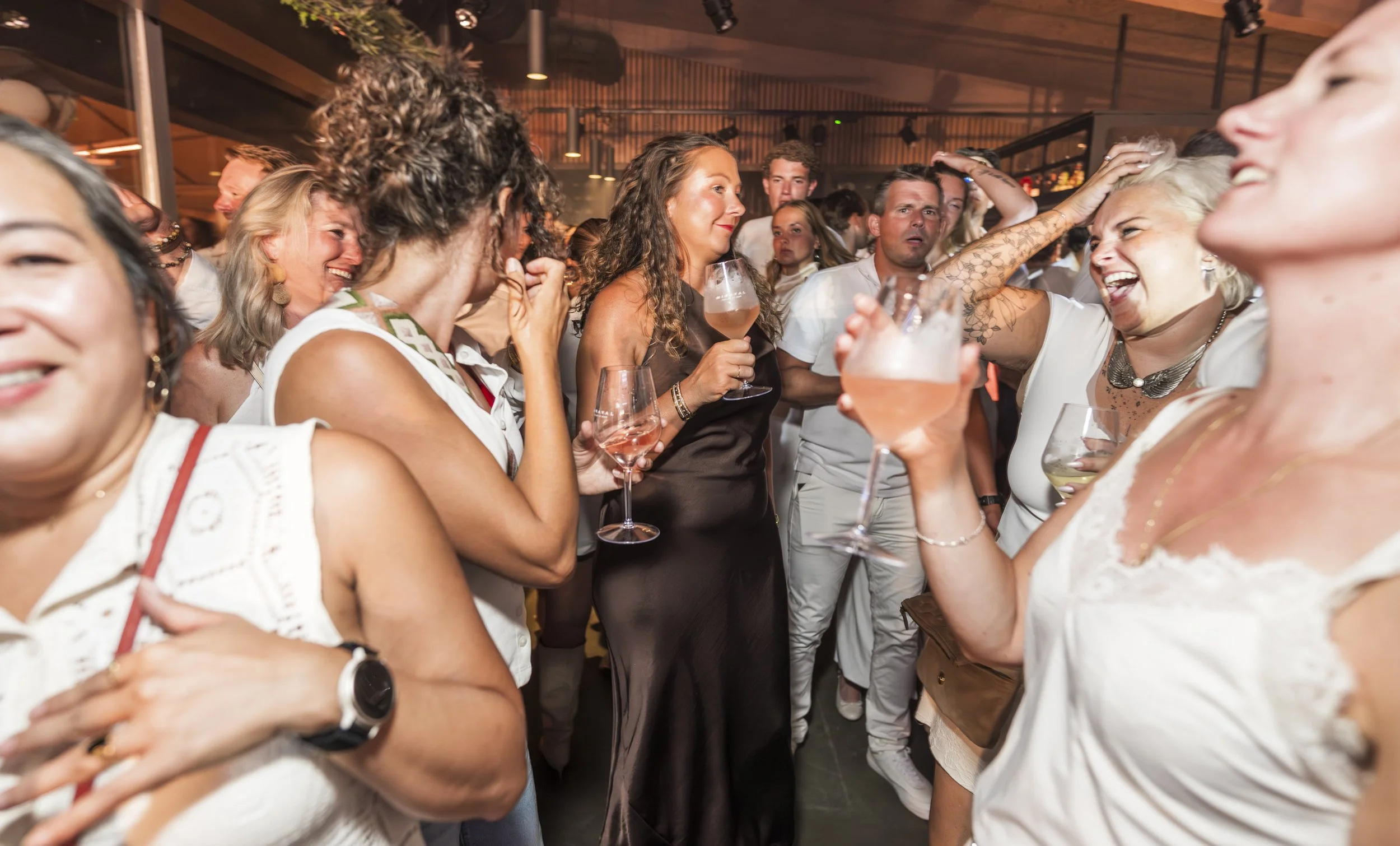 Een groep mensen die samen danst en lacht op een feest of evenement, sommige drinken wijn.