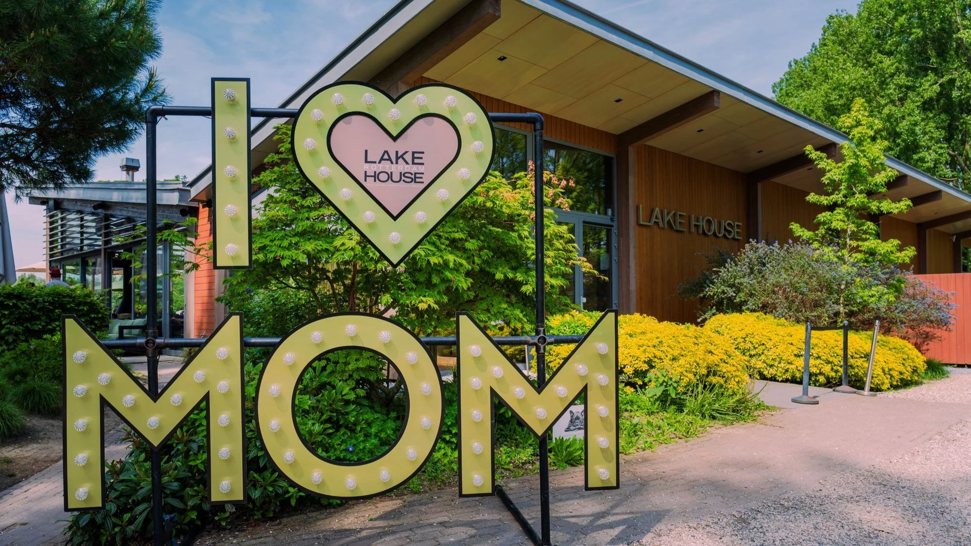Een marquee met de woorden 'I ♥ MØN', voor een gebouw genaamd Lake House, met groene planten en bloemen eromheen.