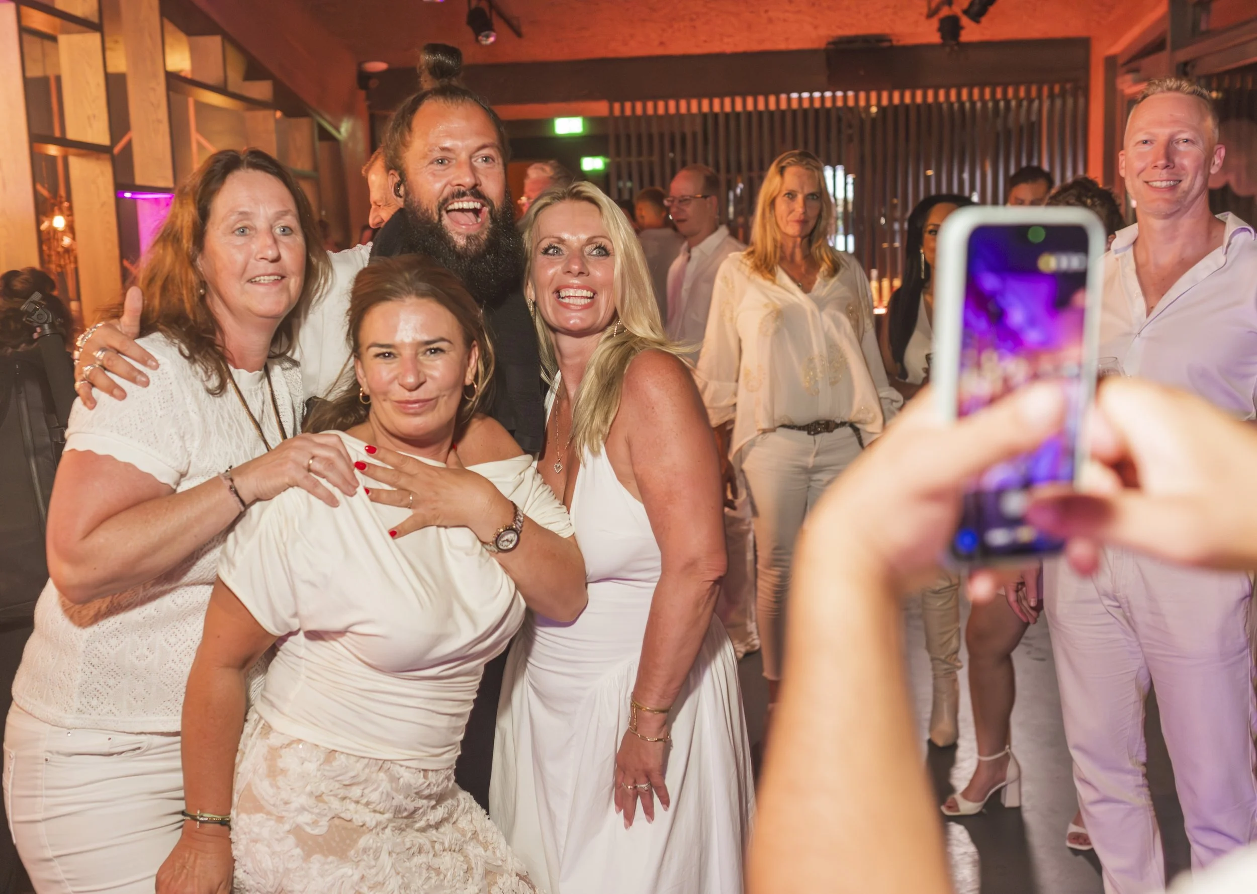 Groep mensen die poseert voor een foto tijdens een feest of evenement in een binnenruimte met houten interieur.