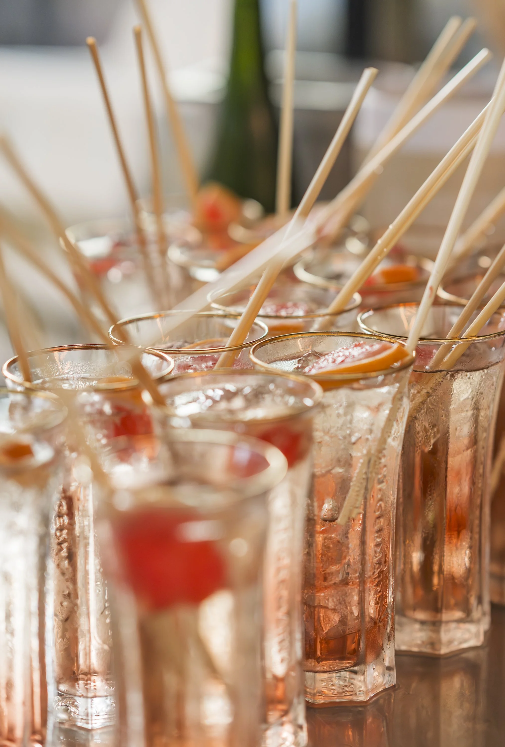 Rioolbuizen met heldere glazen containing roze en oranje cocktails met ijs en rietjes, op een tafel.