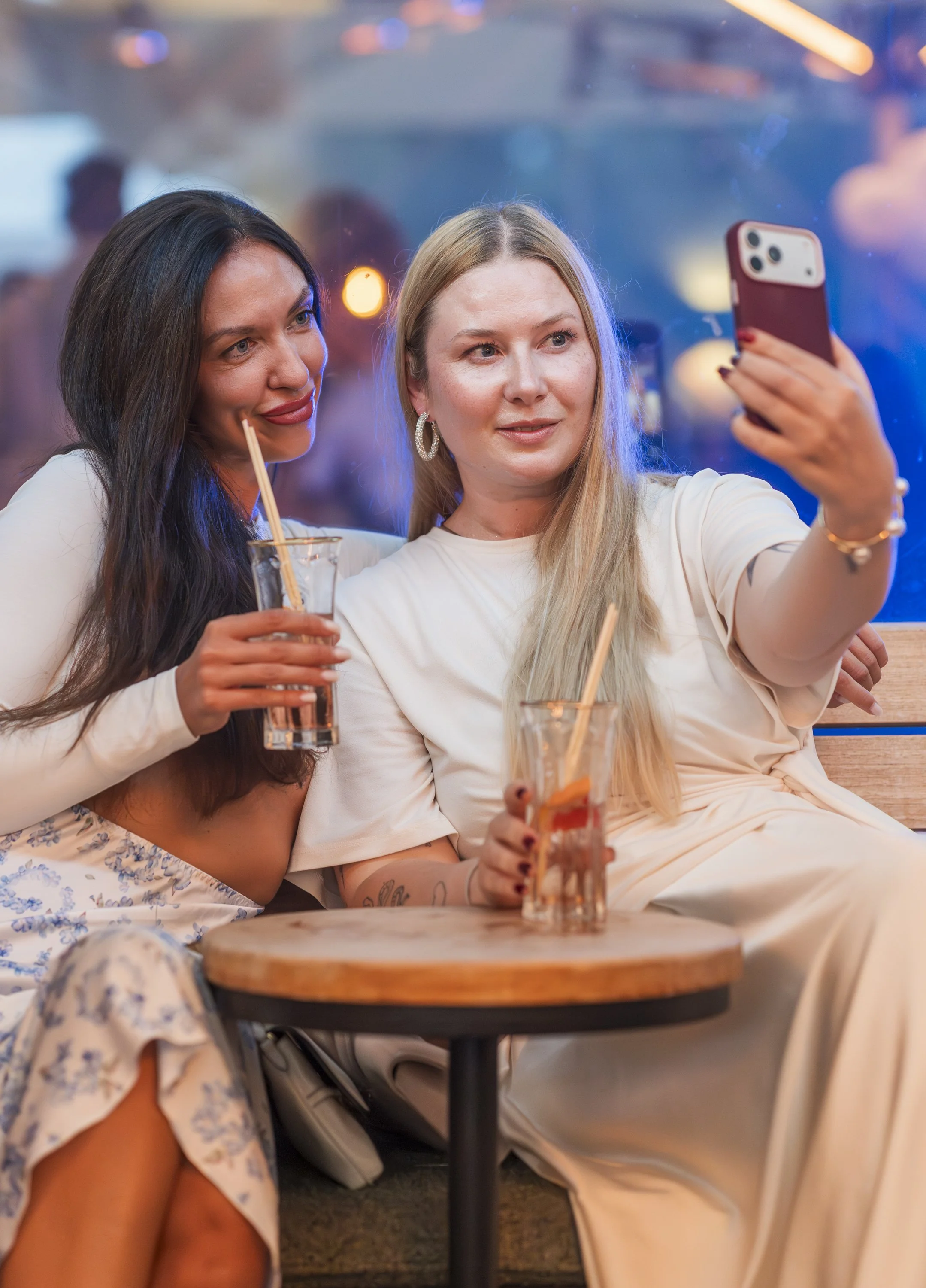 Twee jonge vrouwen maken een selfie in een bar of restaurant, terwijl ze genieten van drankjes met rietjes.
