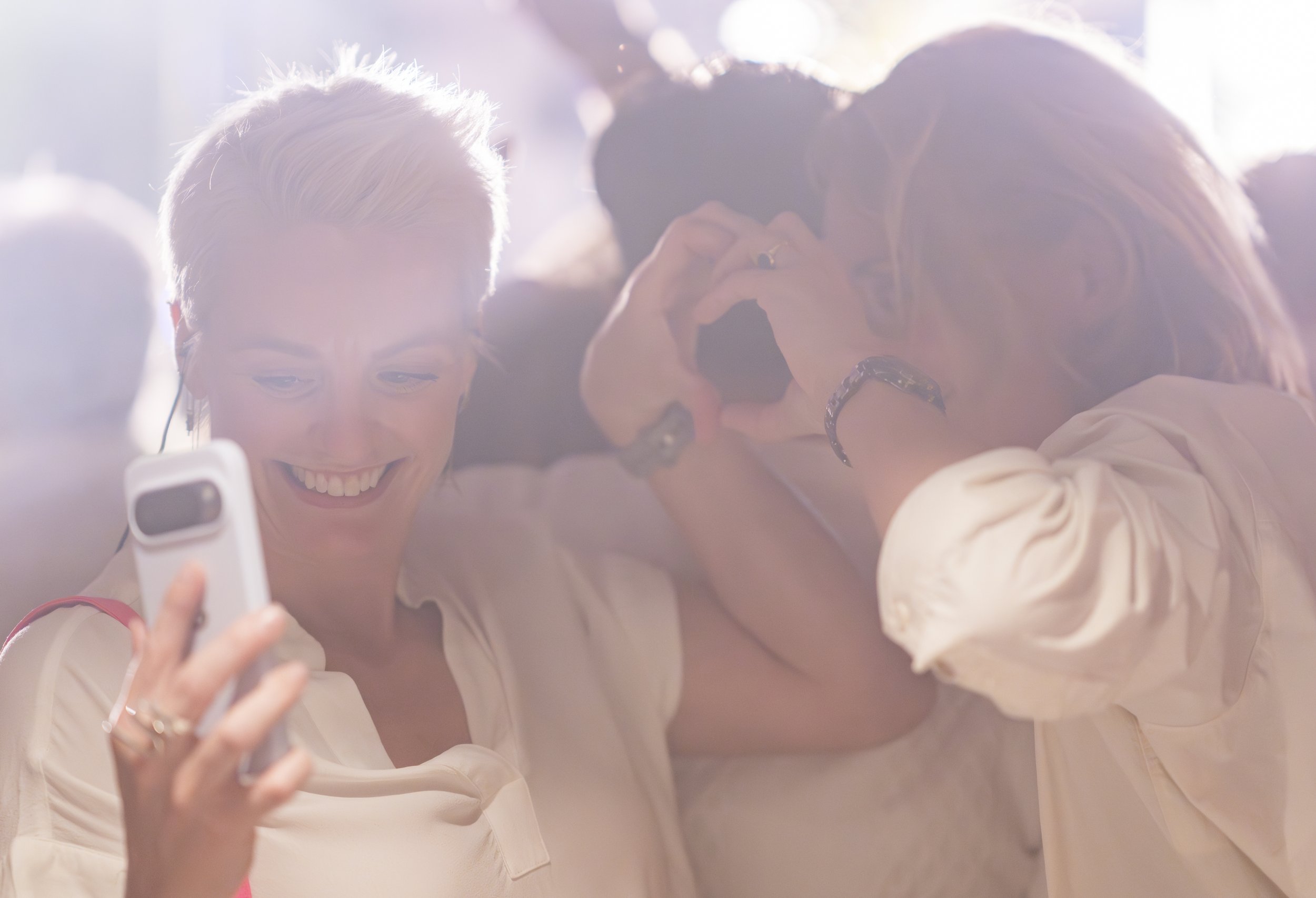 Twee vrouwen maken een selfie samen, lachen en lijken plezier te hebben, onder fel zonlicht.