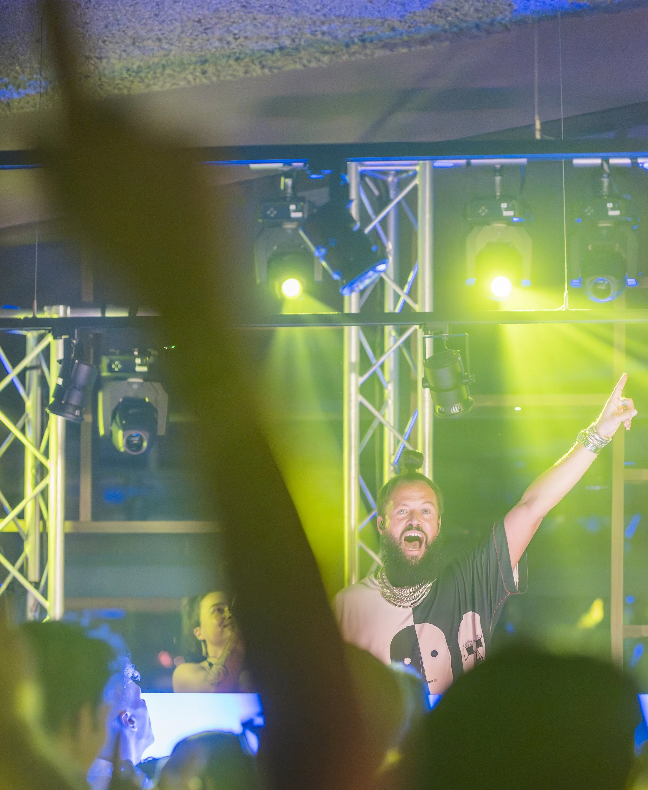 Een man met een beard en een T-shirt met panda print, die enthousiast lijkt te zijn tijdens een evenement of concert met groene en blauwe verlichting.