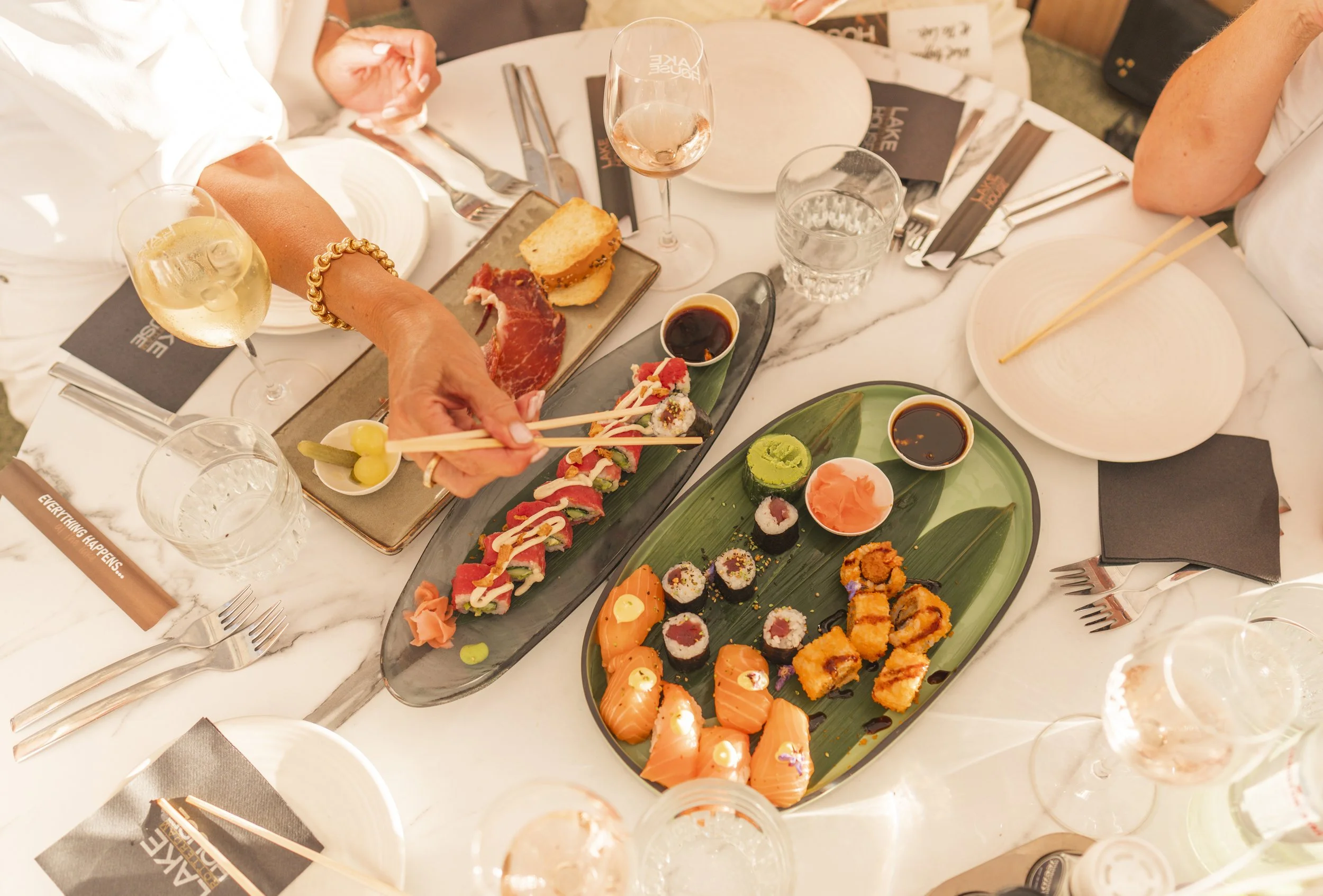 Een tafel met verschillende soorten sushi, sashimi en sushirollen, servies en drinken inclusief wijn en water, klaar voor een feestelijke maaltijd.